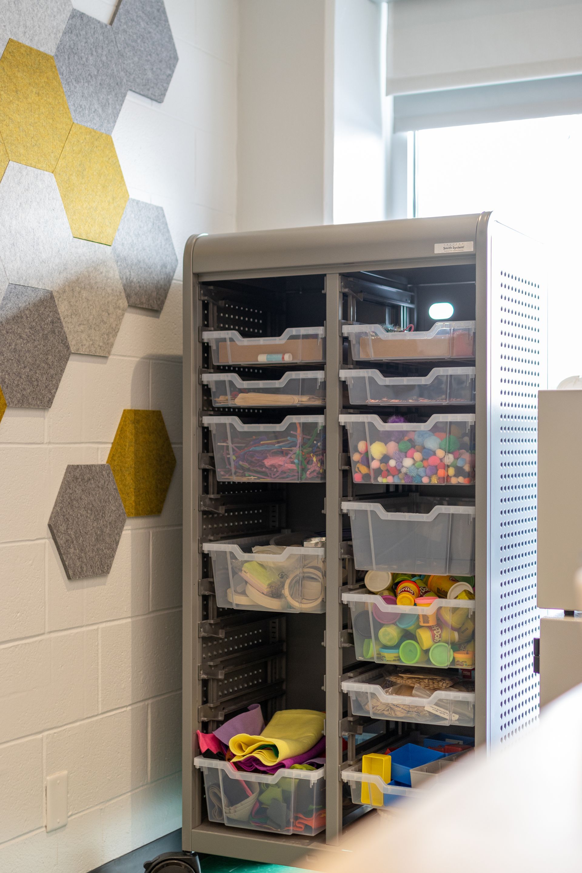 Gray storage unit filled with clear plastic bins. Hexagon wall art is on the left.