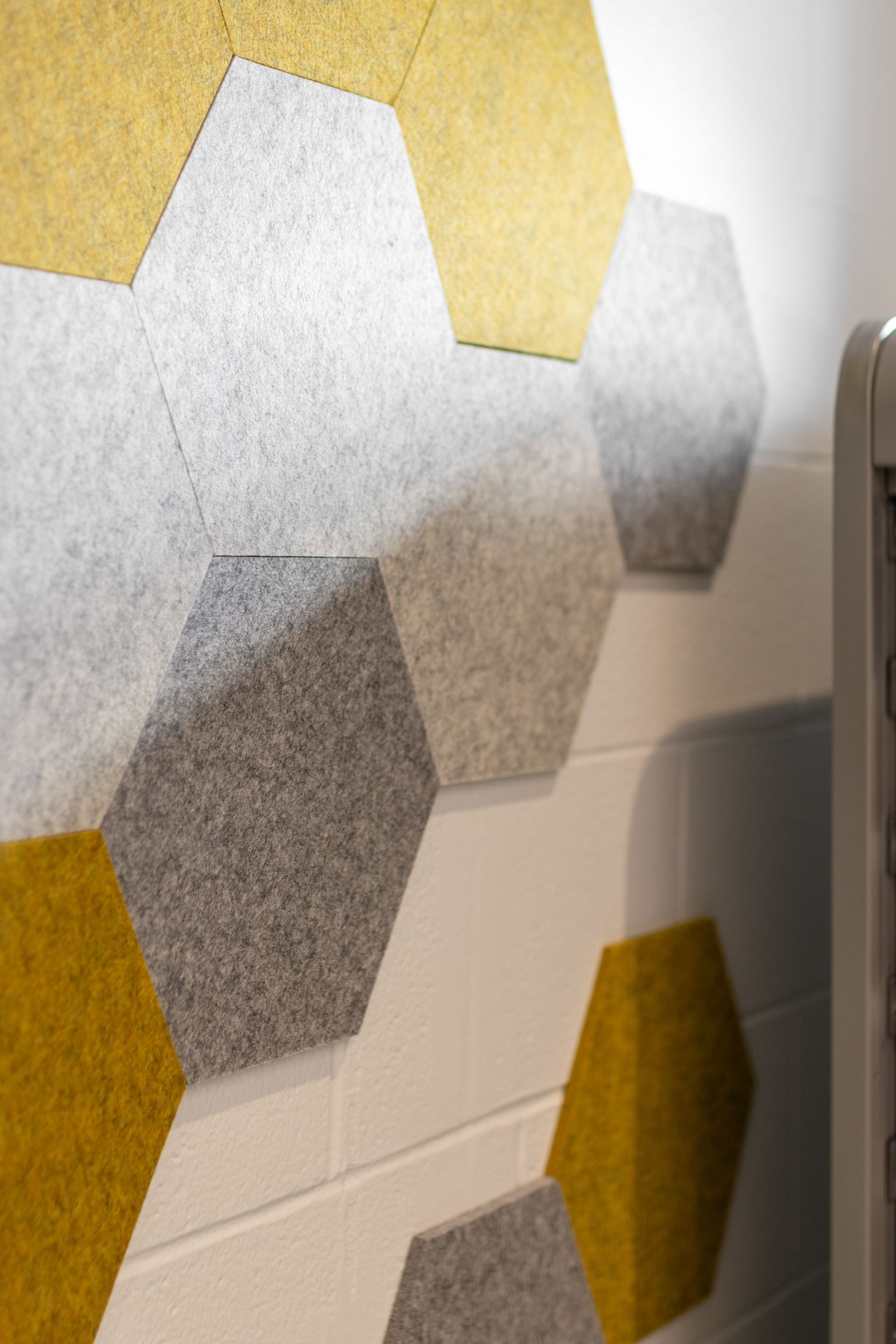 Hexagonal acoustic panels in yellow, gray, and beige on a white wall.
