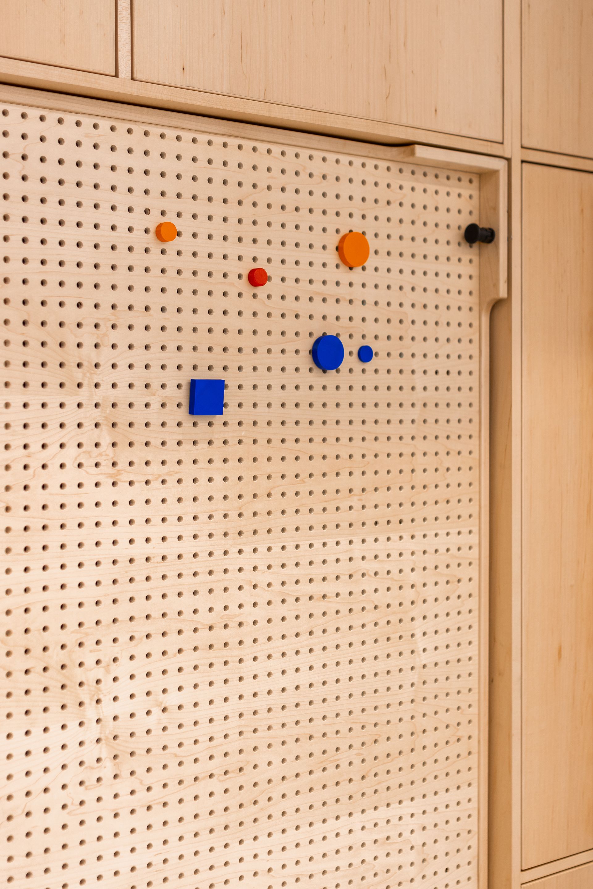 Pegboard with colorful, geometric shapes attached, set into a wooden wall.
