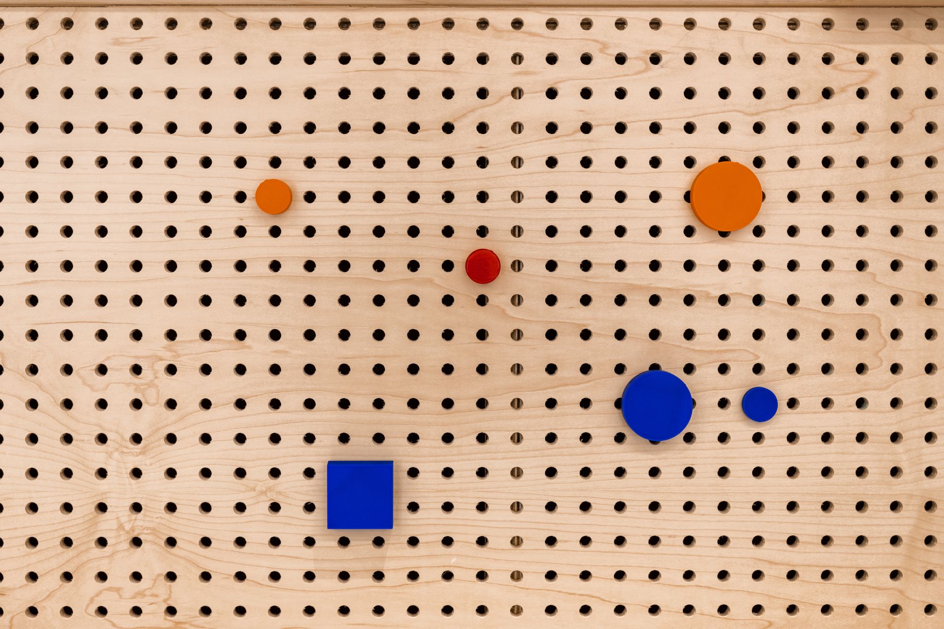 Wooden pegboard with various orange, blue, and red geometric shapes.