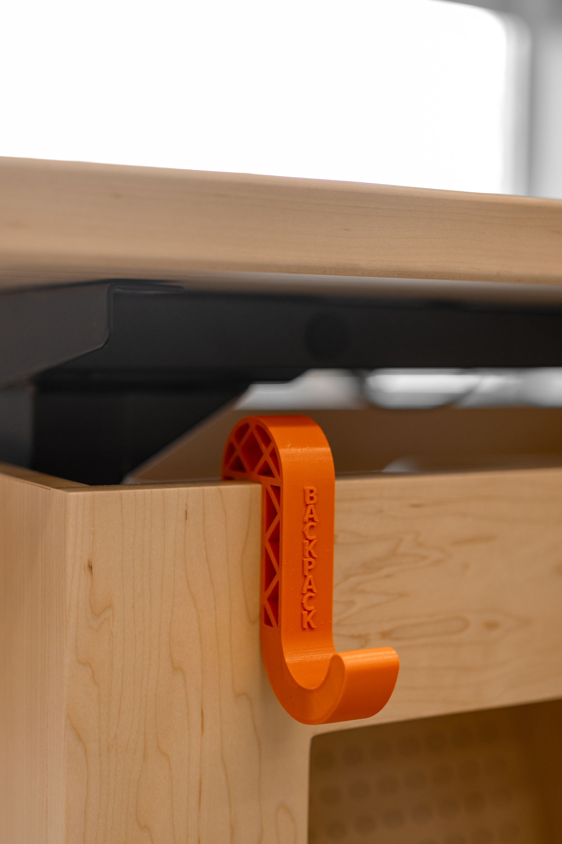 Orange plastic hook hanging on a wooden cabinet, attached to a black table. The hook is labeled