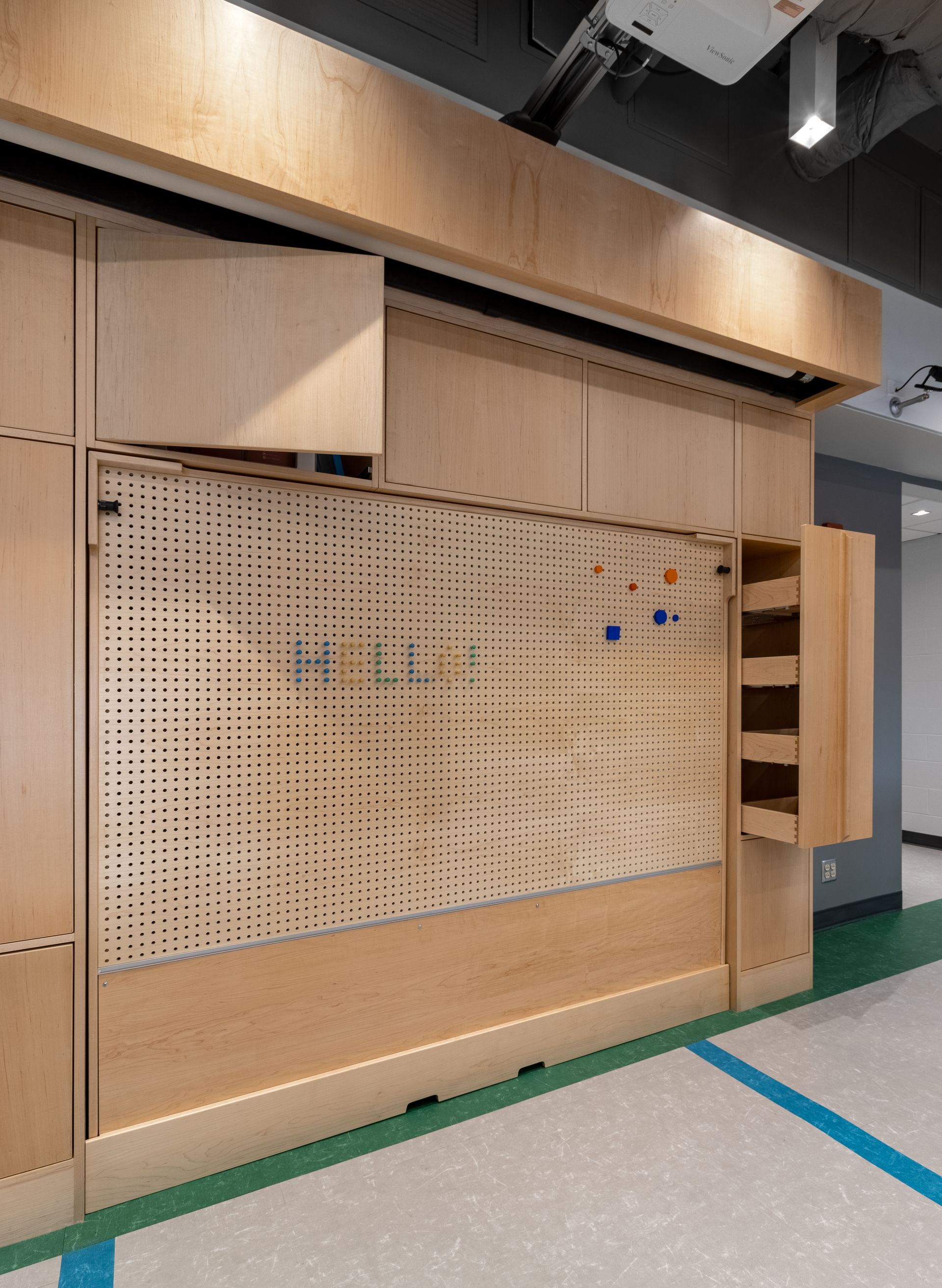 Wooden wall with perforated panel and storage compartments. Blue and green floor.
