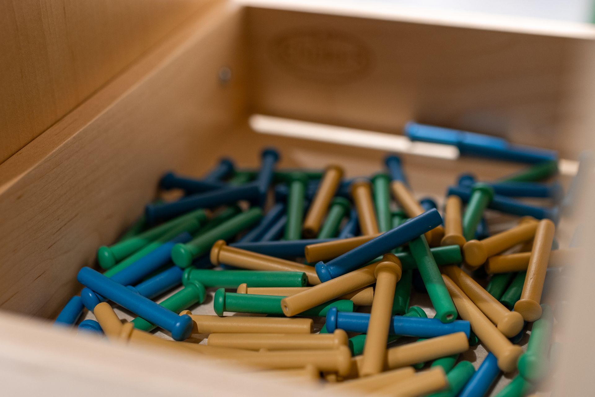 Wooden drawer filled with blue, green, and tan colored peg-shaped pieces.