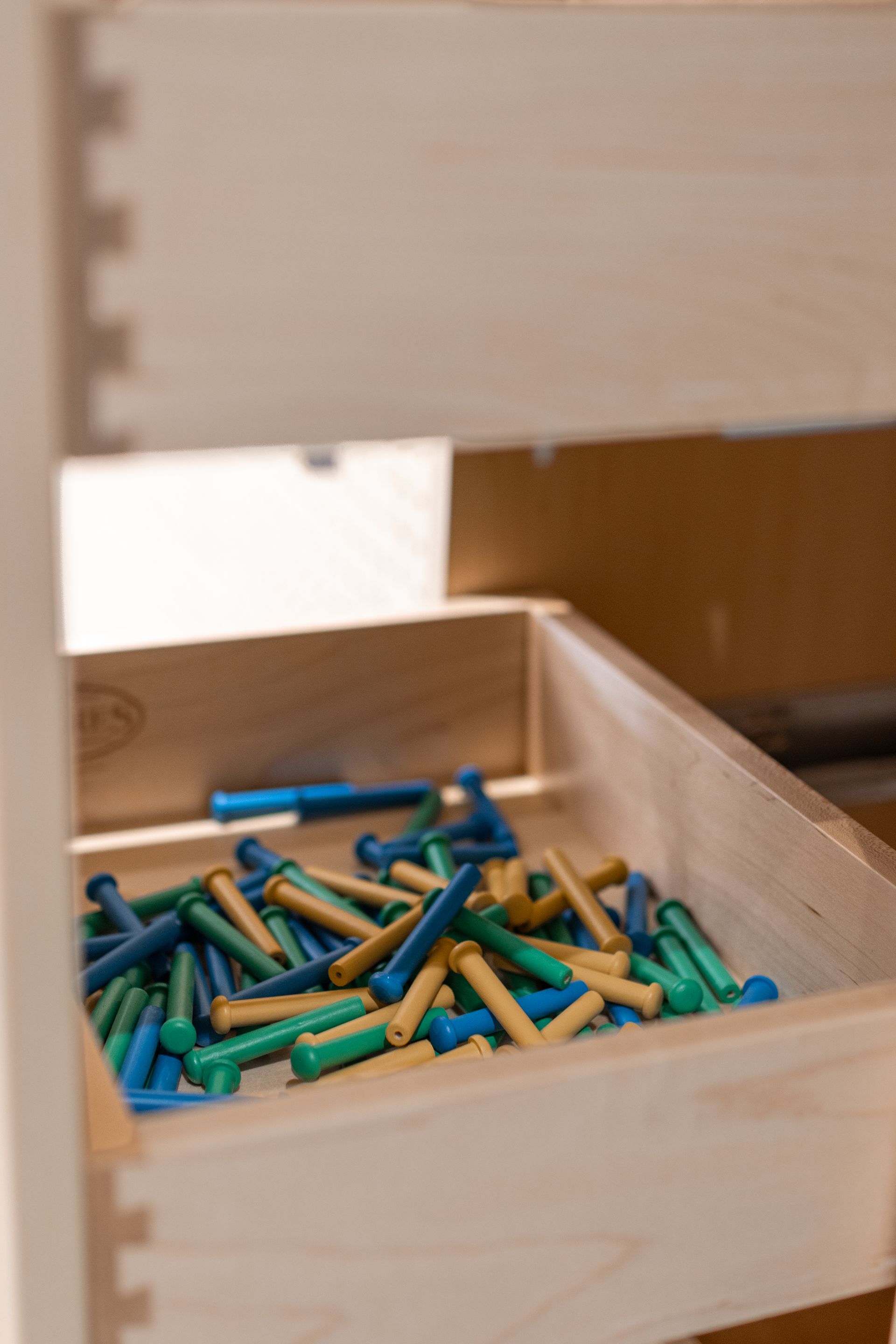 Wooden drawer with a pile of blue, green, and tan cylindrical objects.