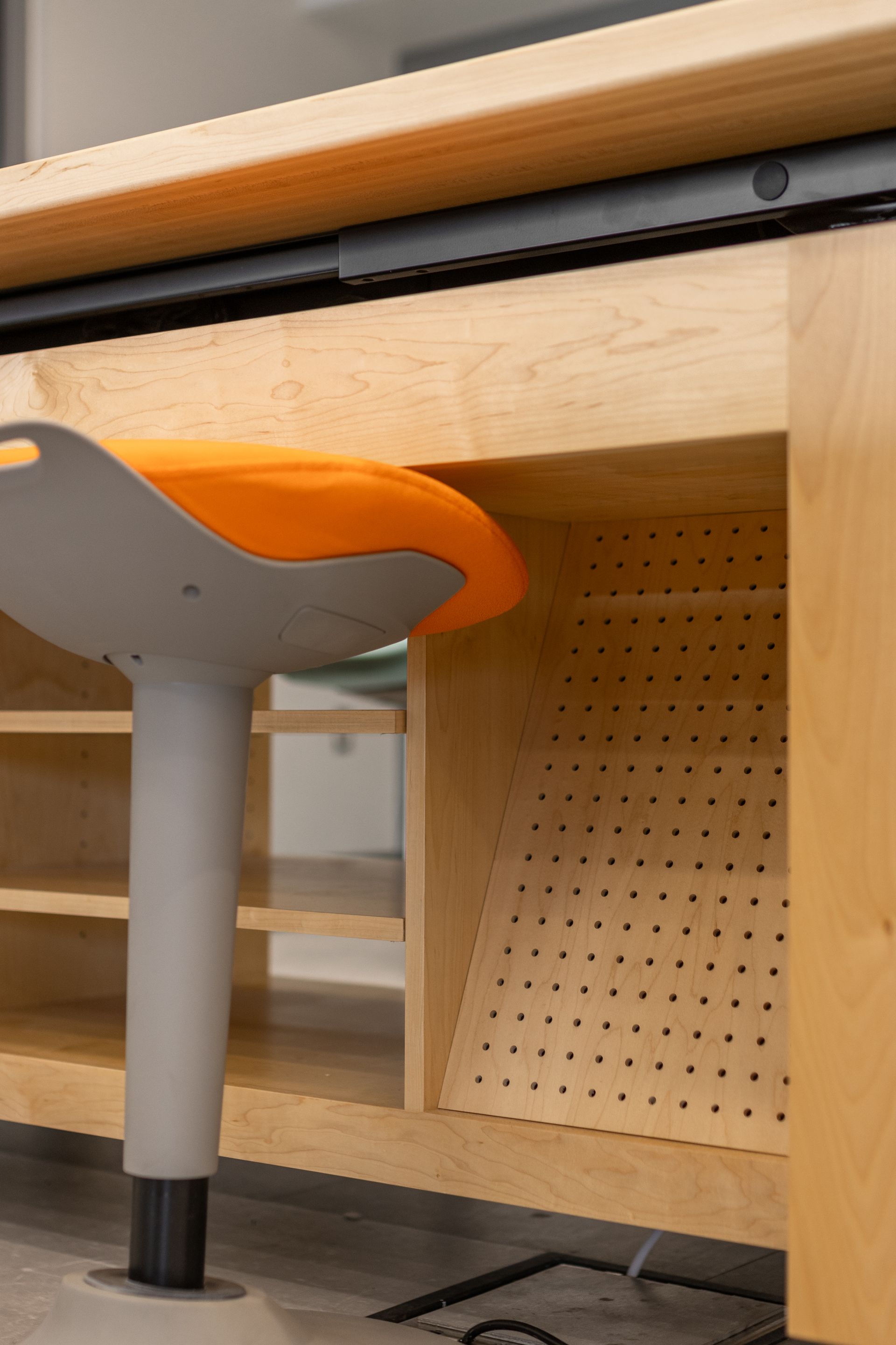 Orange and gray stool at a wooden workstation with shelves and a perforated panel.