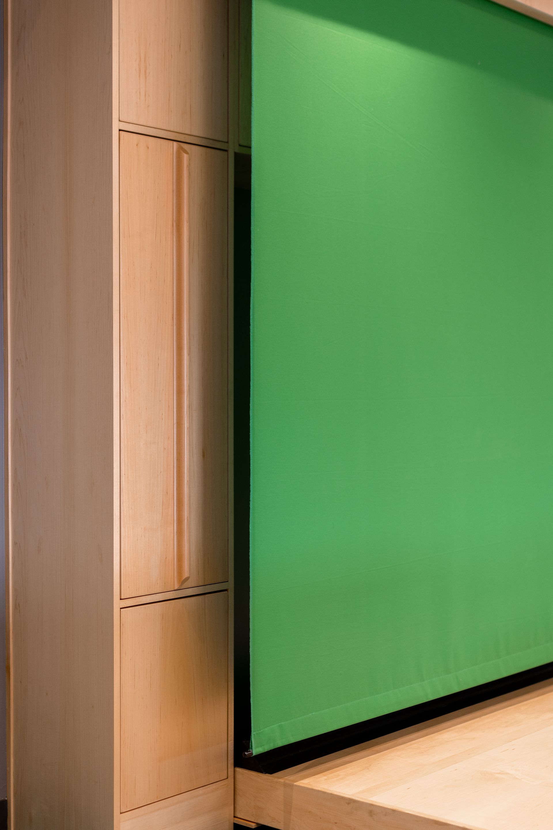 Wooden cabinet beside a green screen. The screen is lowered, and the cabinet is light-colored wood.