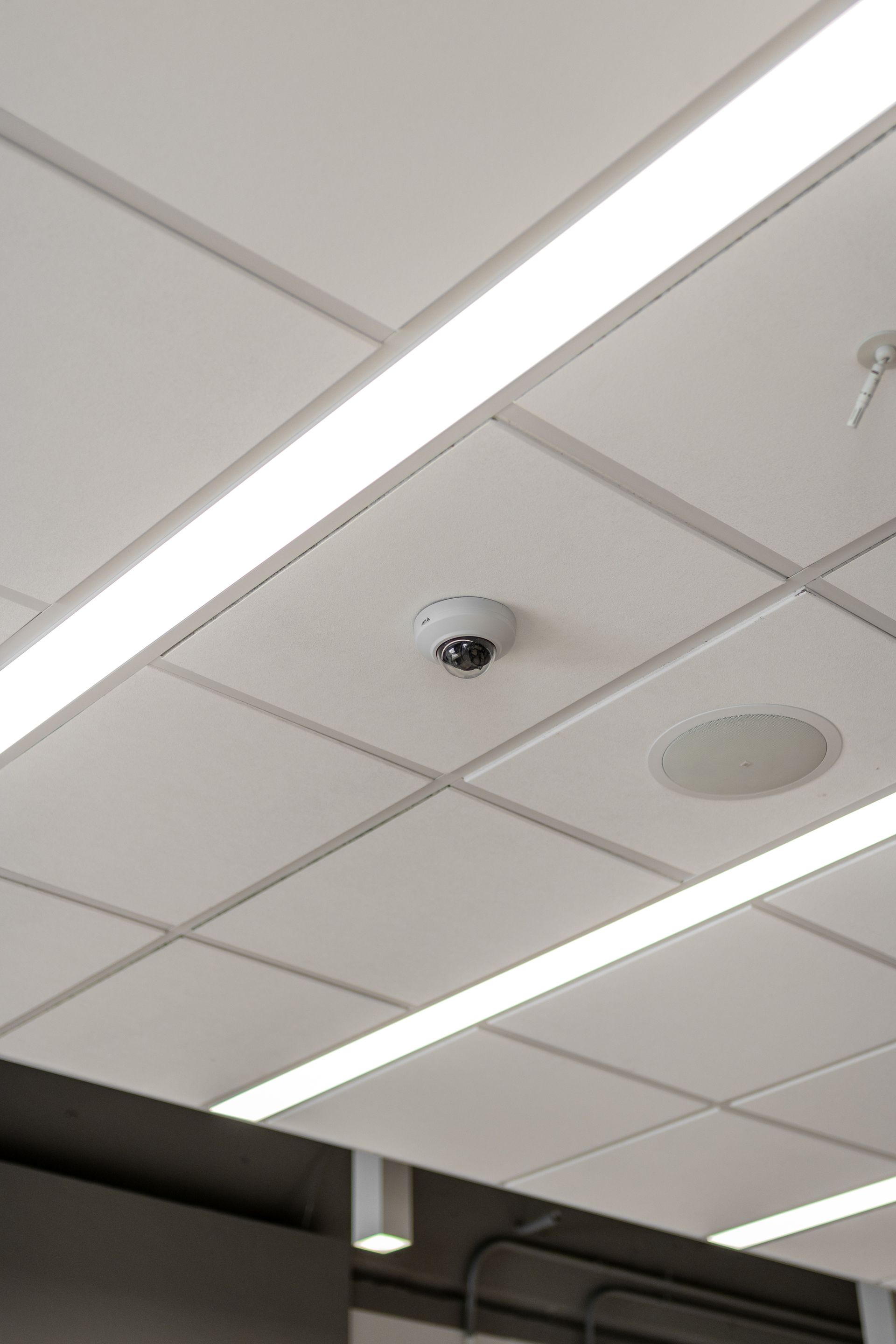 Security camera mounted on a white ceiling with recessed lighting.