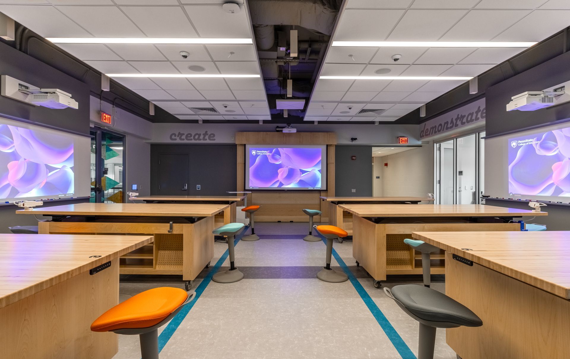 Modern classroom with lab tables and colorful stools, screens on walls, and a large projection screen.