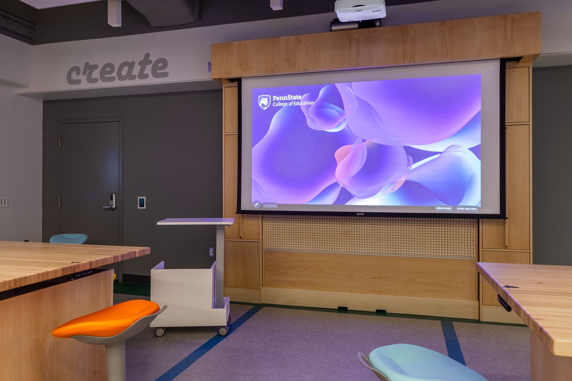 Classroom with projection screen displaying purple abstract shapes, orange and blue stools.