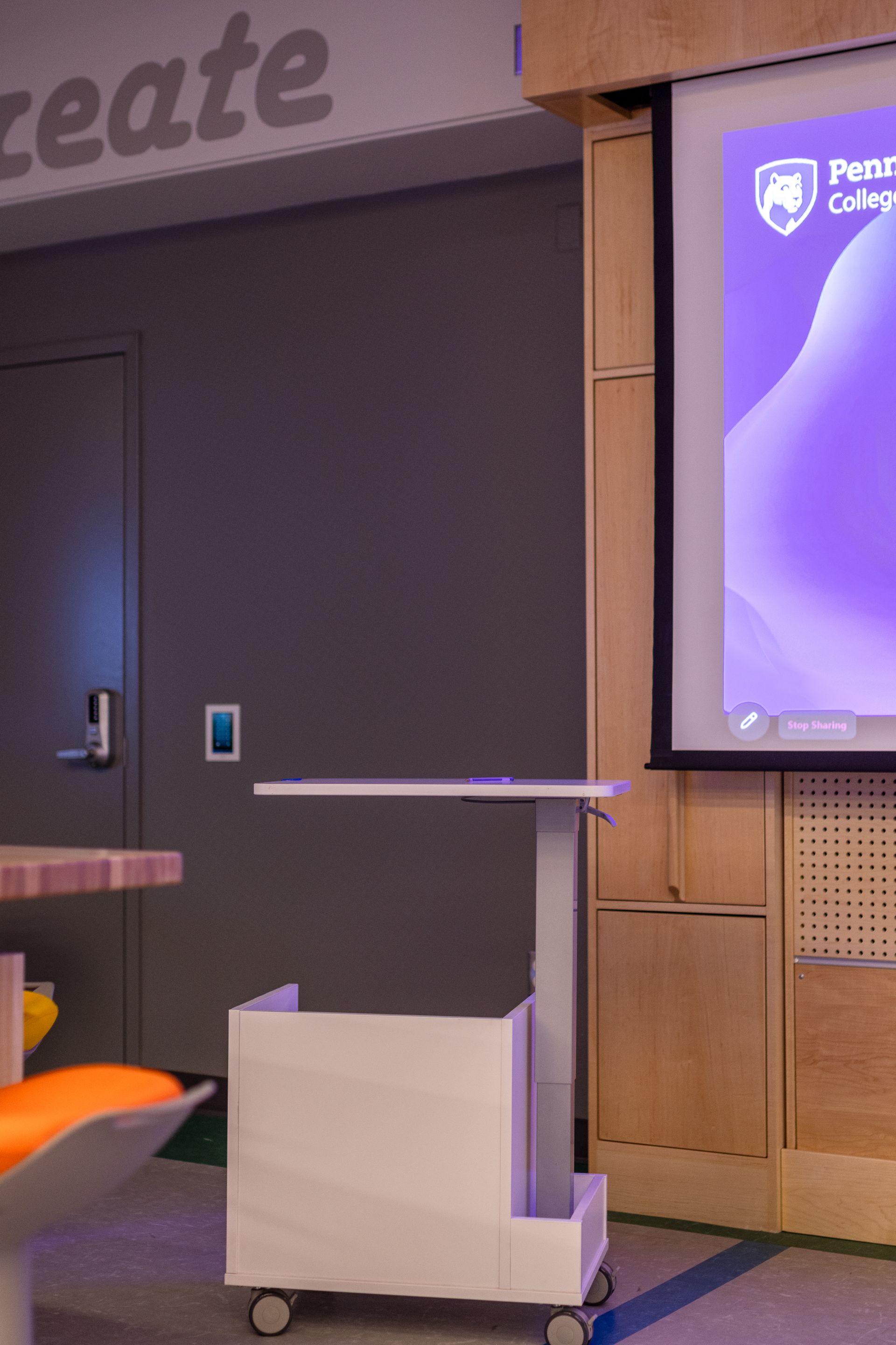 White presentation cart on wheels in front of a projection screen; door on the left; create text on wall.