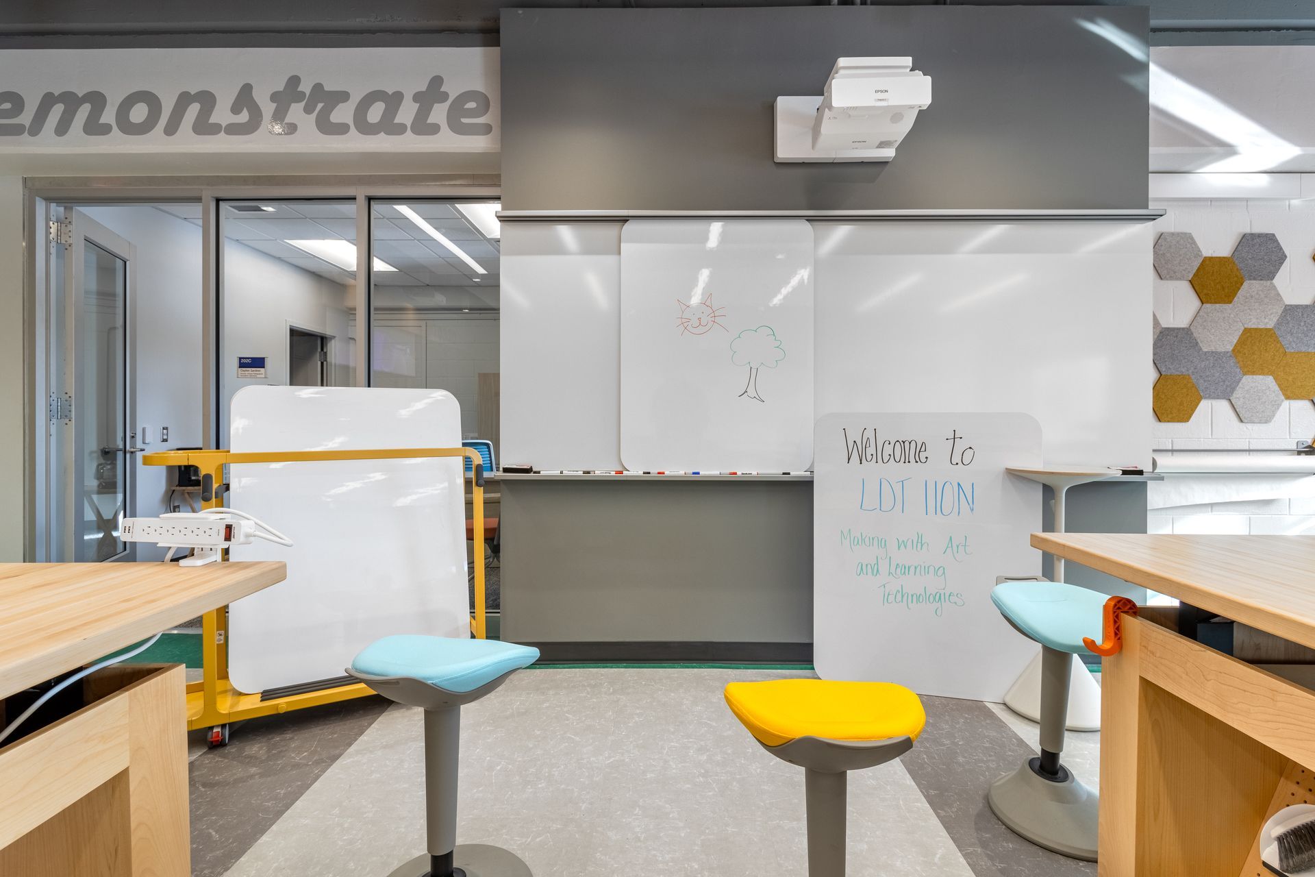 Classroom with whiteboards, colorful stools, tables, and a projector.