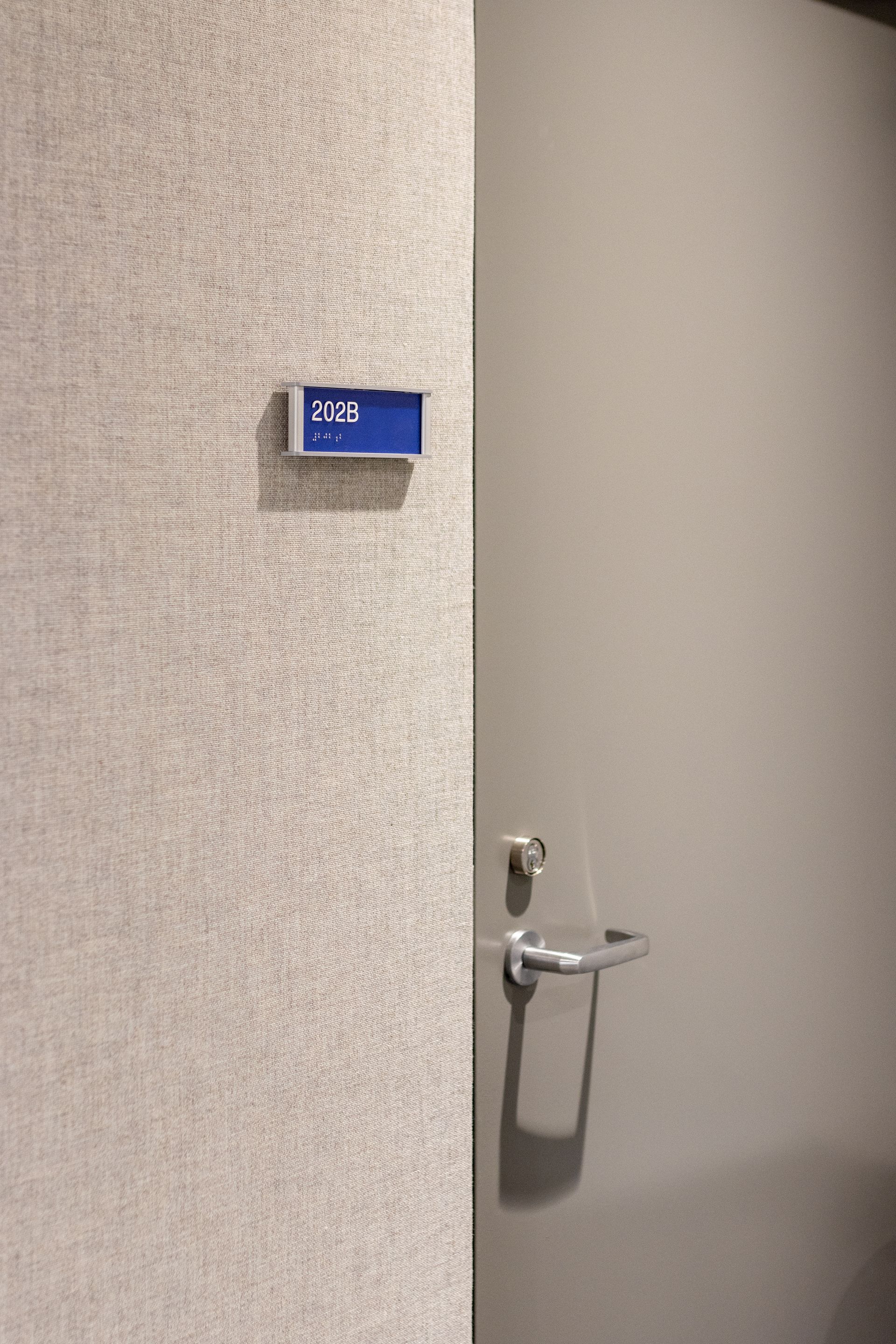 Door with a blue room number sign featuring braille on the left. A silver handle and lock are on the right.