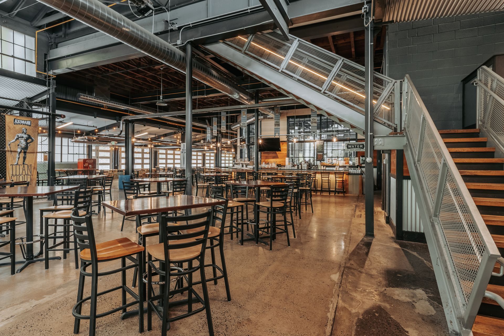 Interior view of a modern restaurant with tables, chairs, and a staircase. Metal and wood construction.