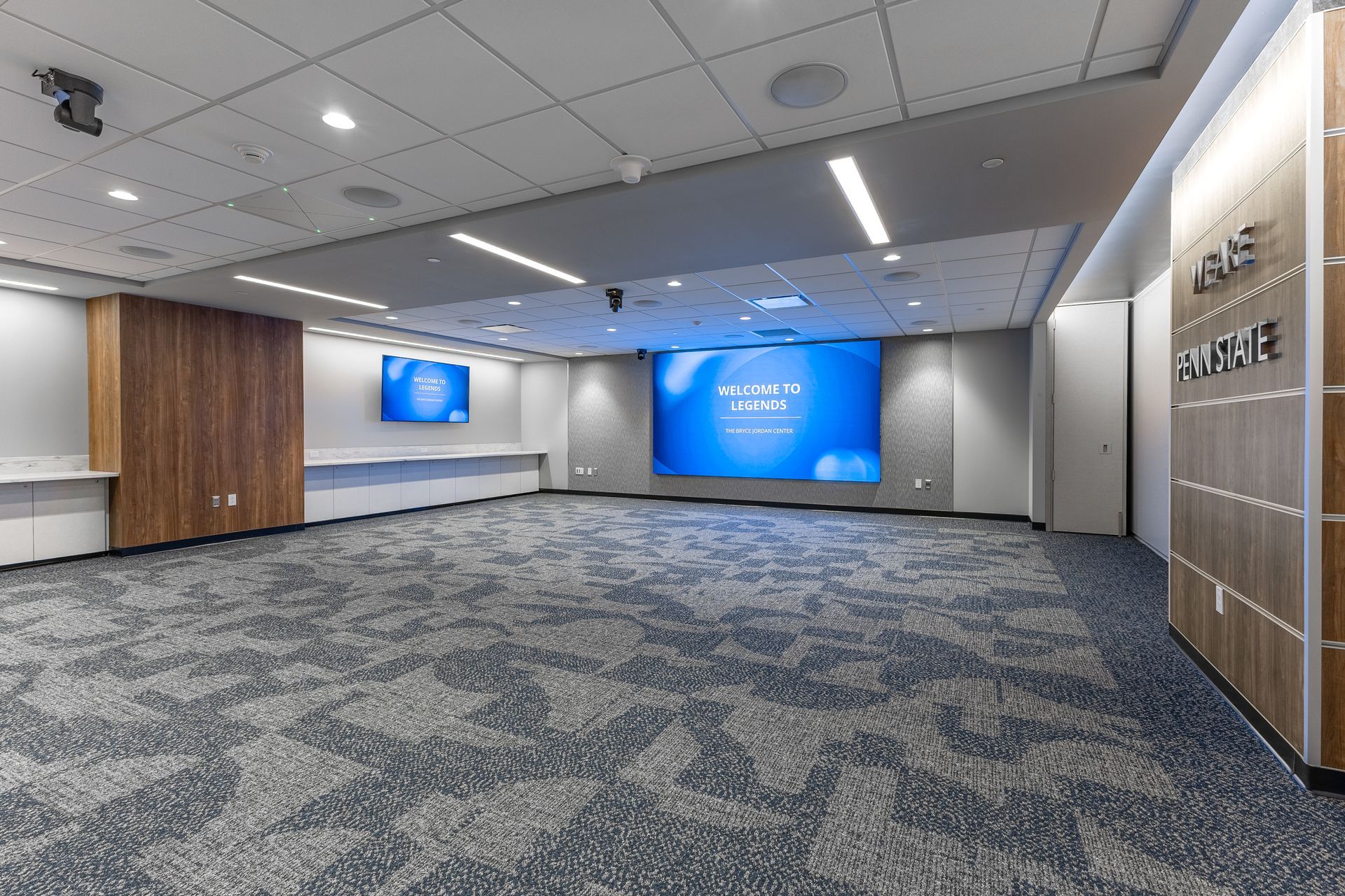Bryce Jordan Center's modern lobby with blue carpet, wood accents, and large digital display screens