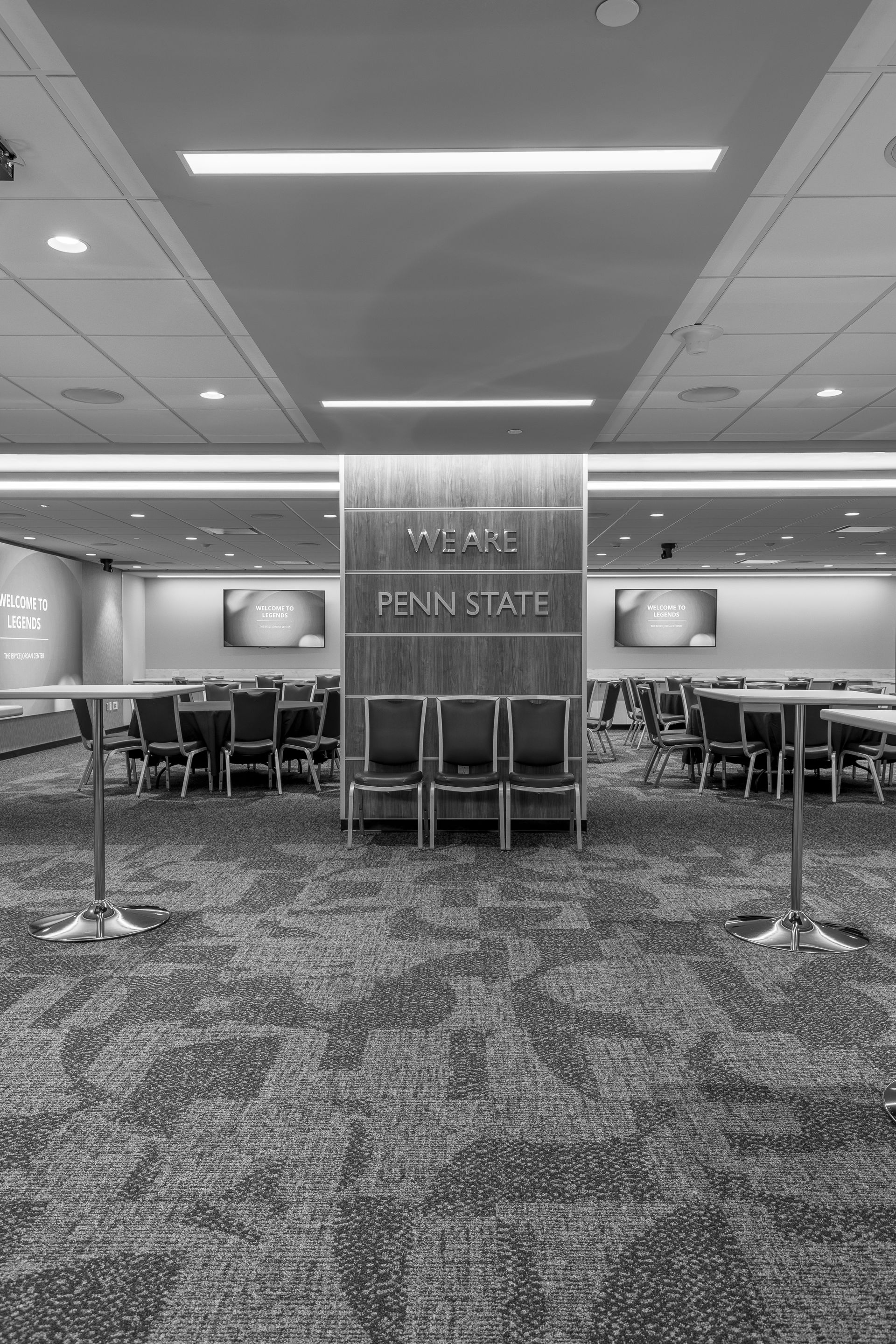 Bryce Jordan Center's empty conference room with carpeted floor, chairs, and a central pillar under fluorescent ceiling lights.