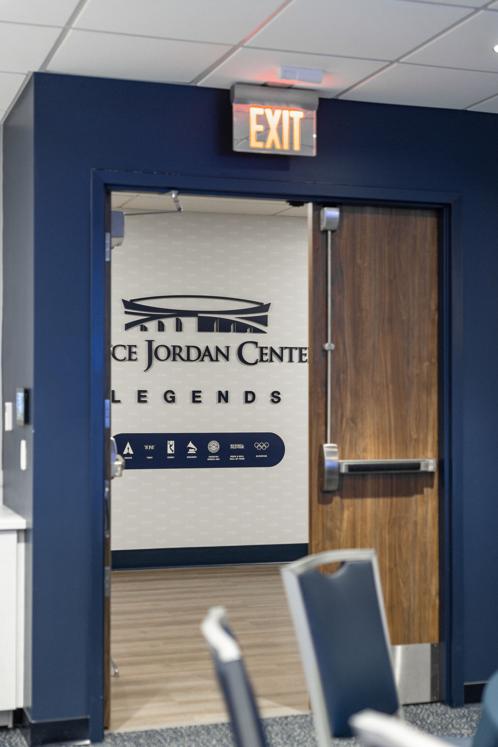 Bryce Jordan Center's hallway exit door with glowing EXIT sign and Jordan Center wall sign behind it