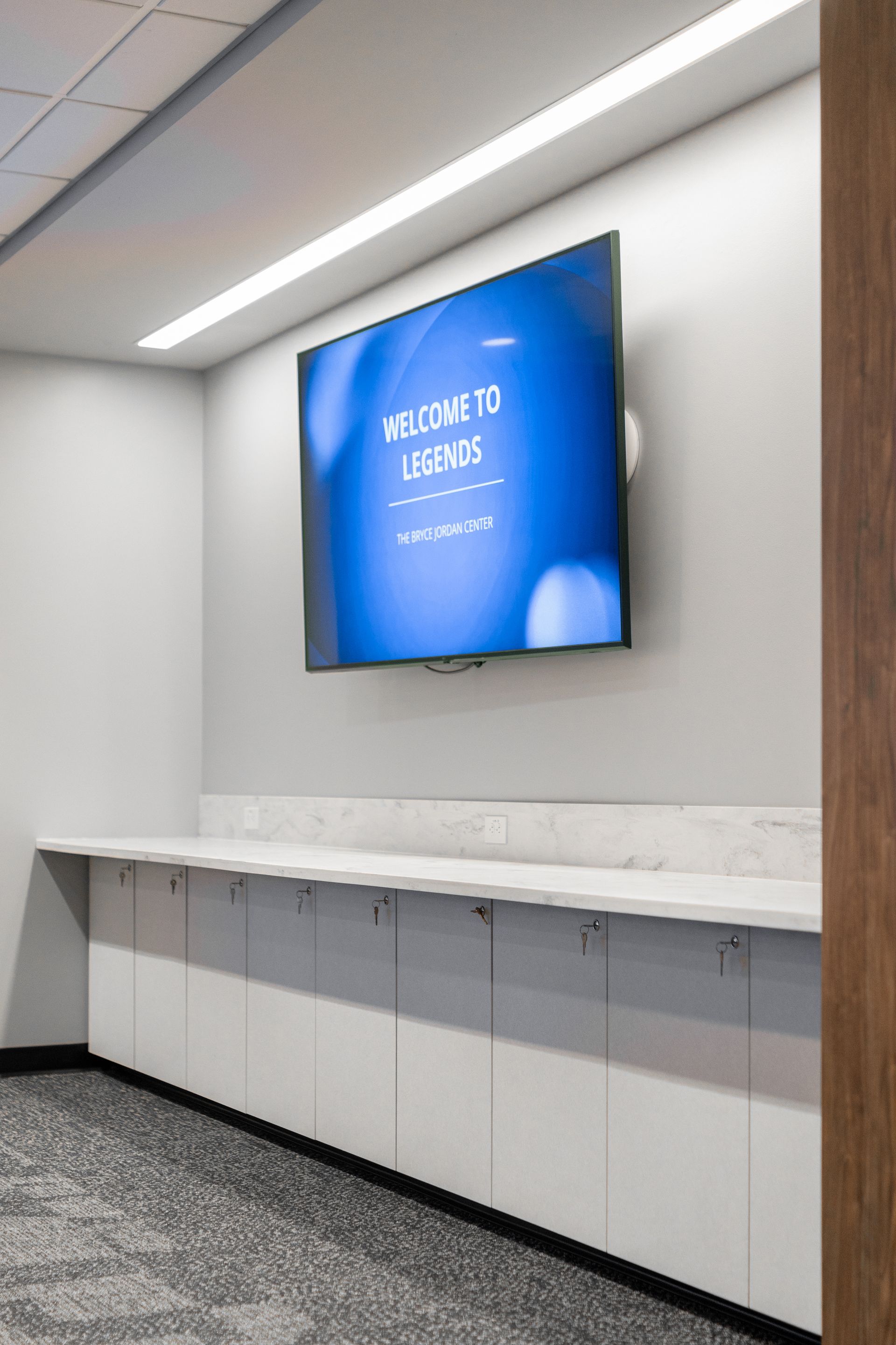 Bryce Jordan Center's modern lobby with a wall-mounted blue display and white countertop cabinets