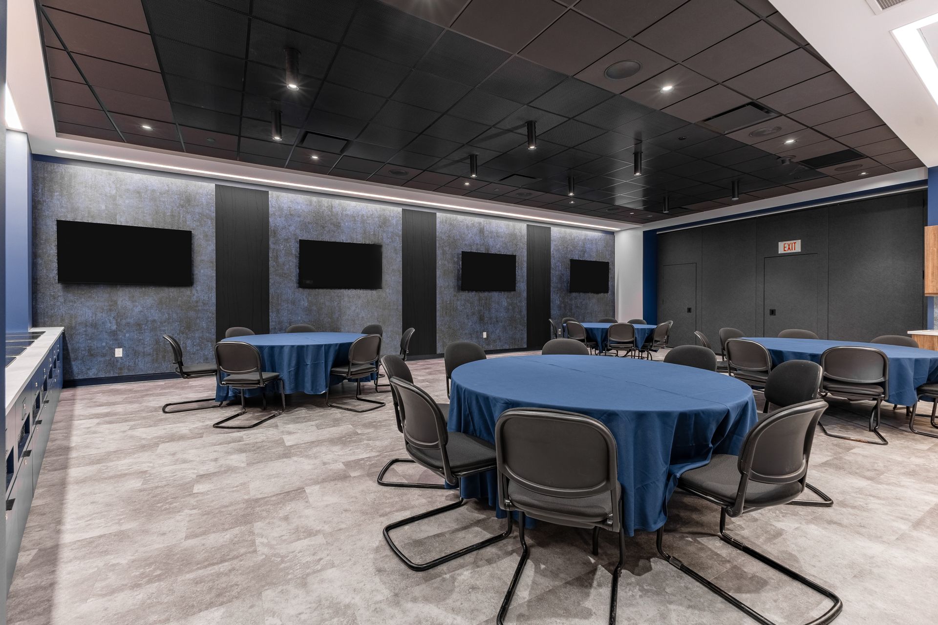 Bryce Jordan Center's modern conference room with round tables, chairs, wall-mounted screens, and dark ceiling panels