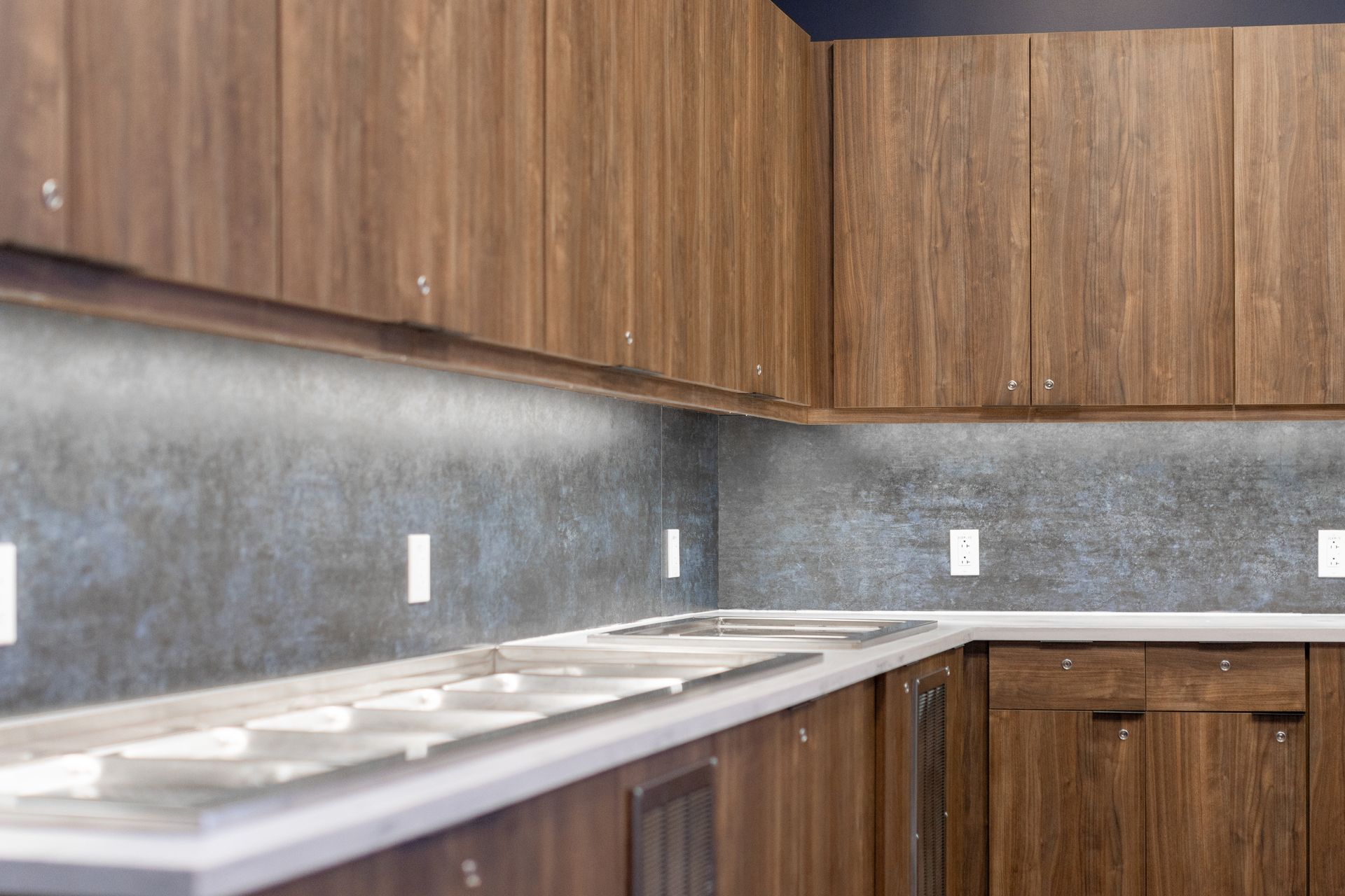 Bryce Jordan Center's empty kitchen with wood cabinets, gray backsplash, and white countertop lighting fixtures