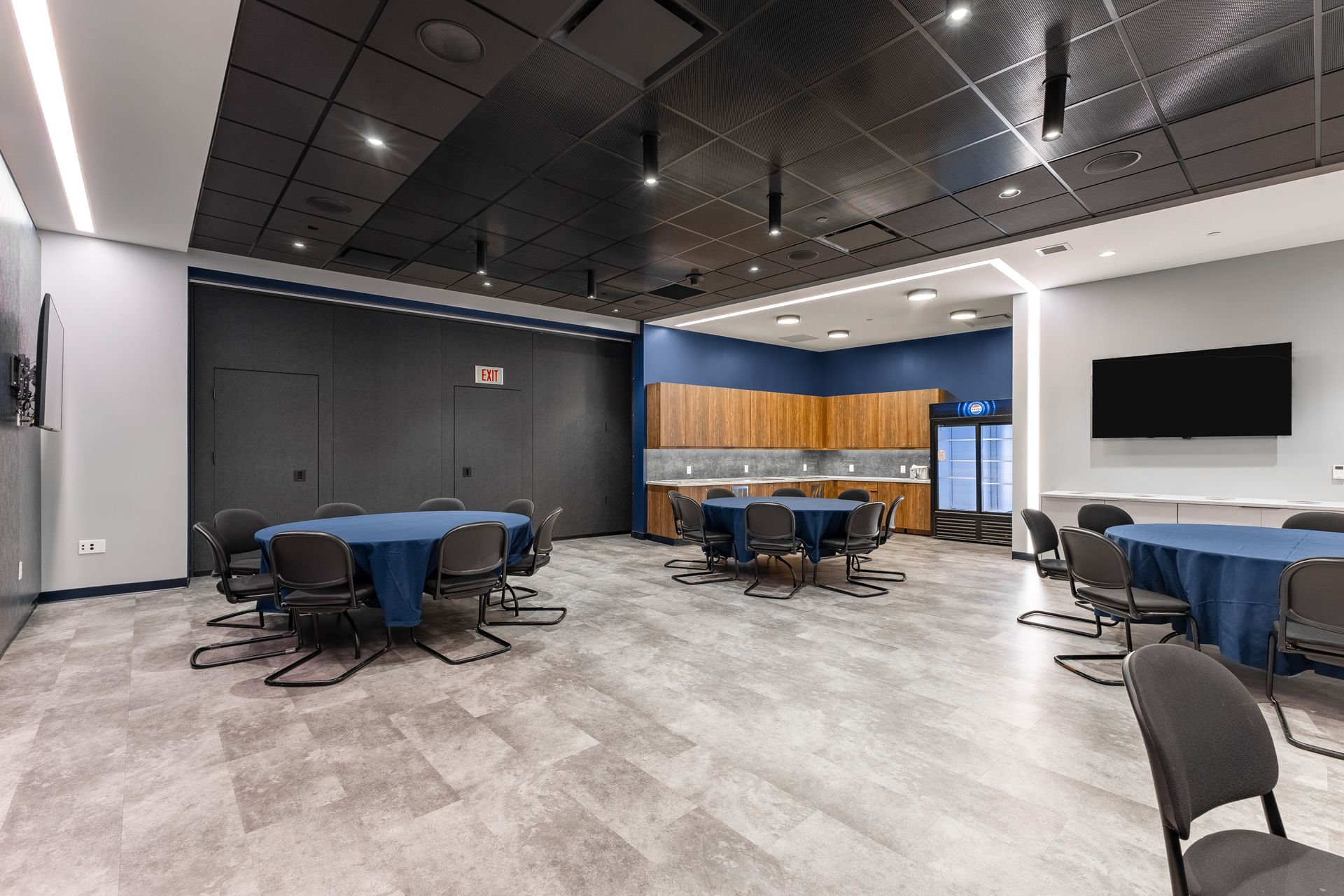 Bryce Jordan Center's modern meeting room with round tables, blue chairs, wood-accent wall, and wall-mounted TV