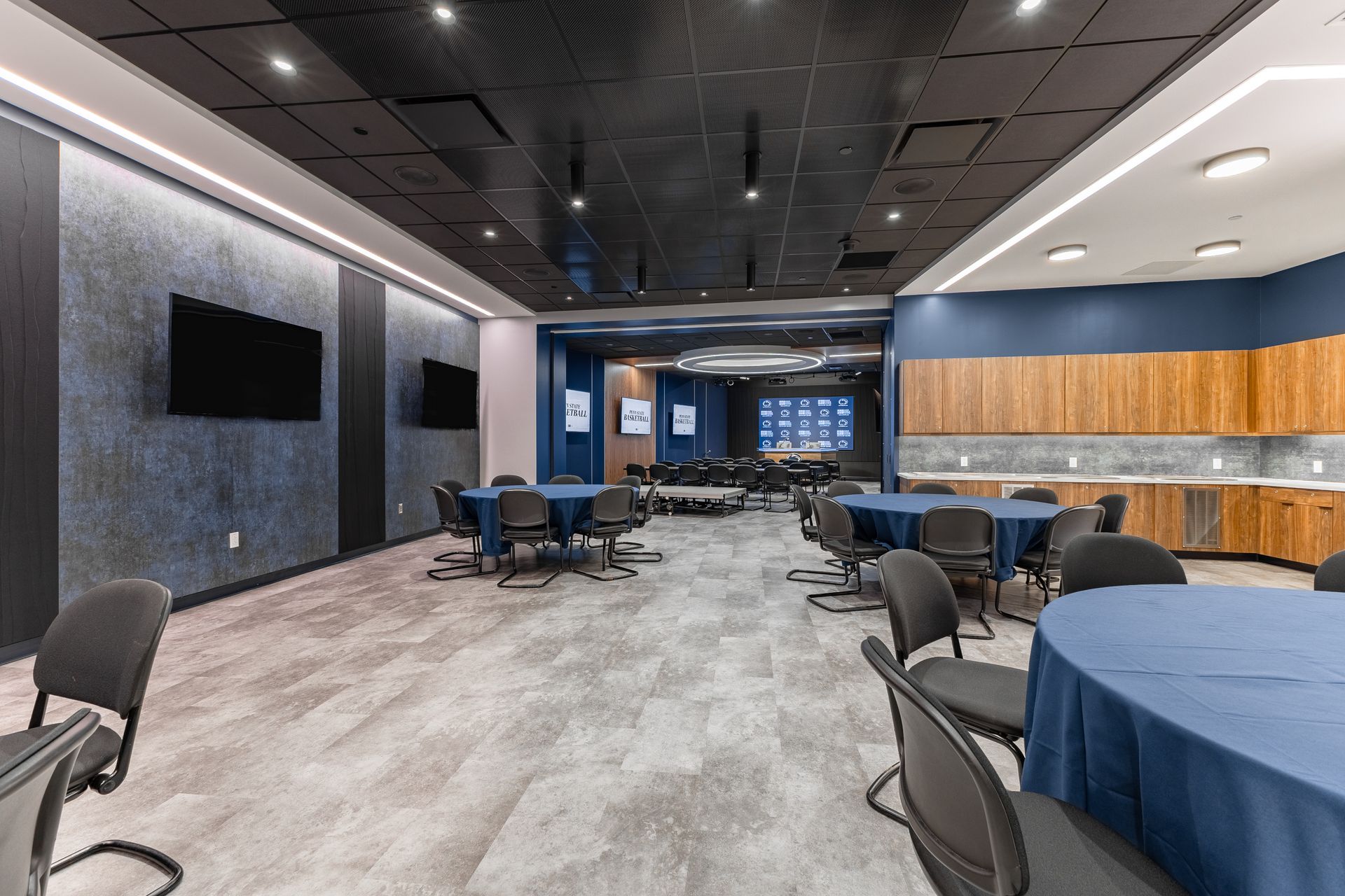 Bryce Jordan Center's modern event hall with round tables, chairs, wood-paneled walls, and a dark ceiling with lights