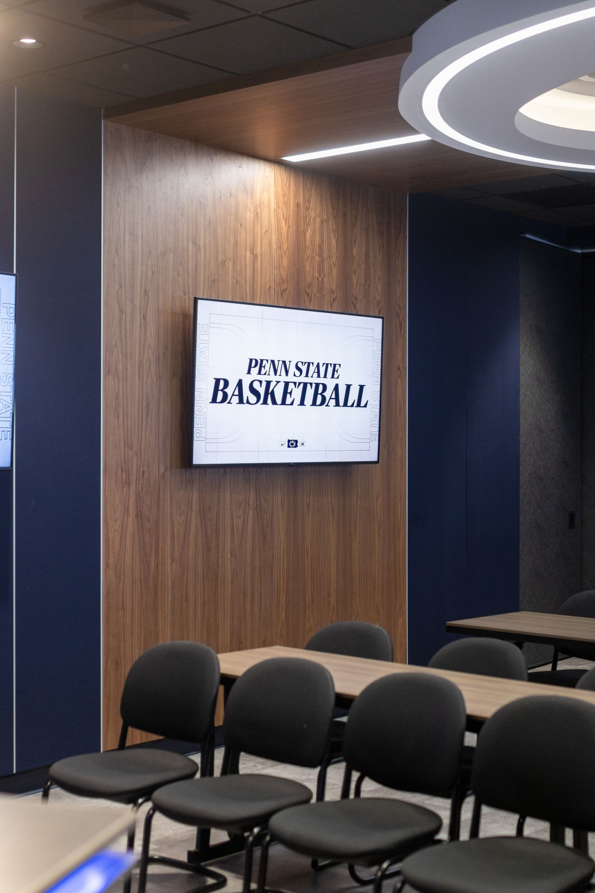 Bryce Jordan Center's conference room with rows of black chairs and a wall-mounted TV displaying a logo on wood paneling.