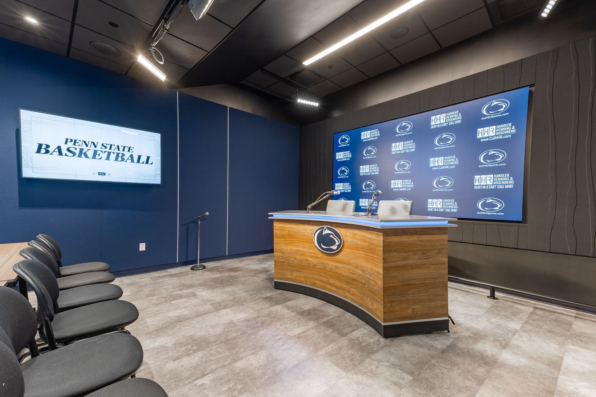 Bryce Jordan Center's modern blue press conference room with podium, logo screen, chairs, and sponsor backdrop