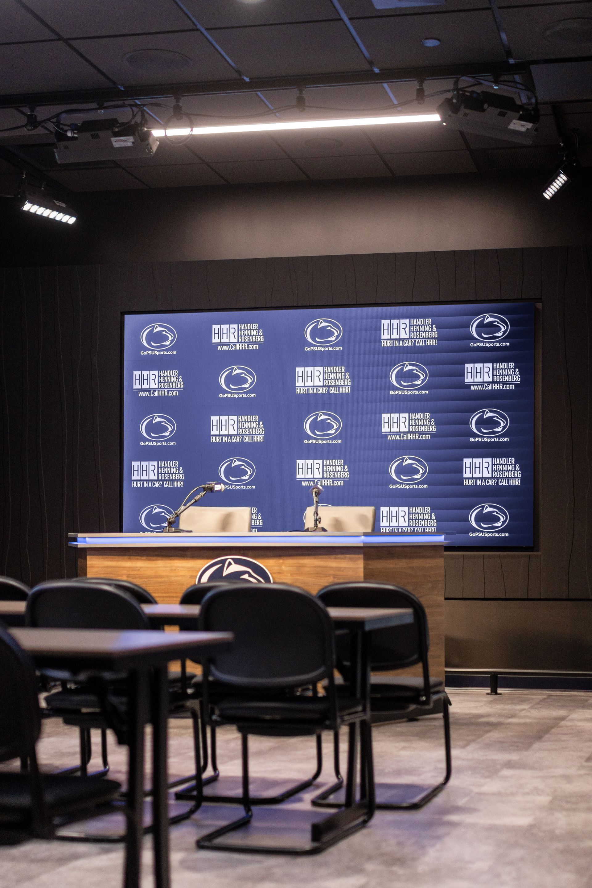 Bryce Jordan Center's empty conference room with tables and chairs in front of a large blue presentation screen