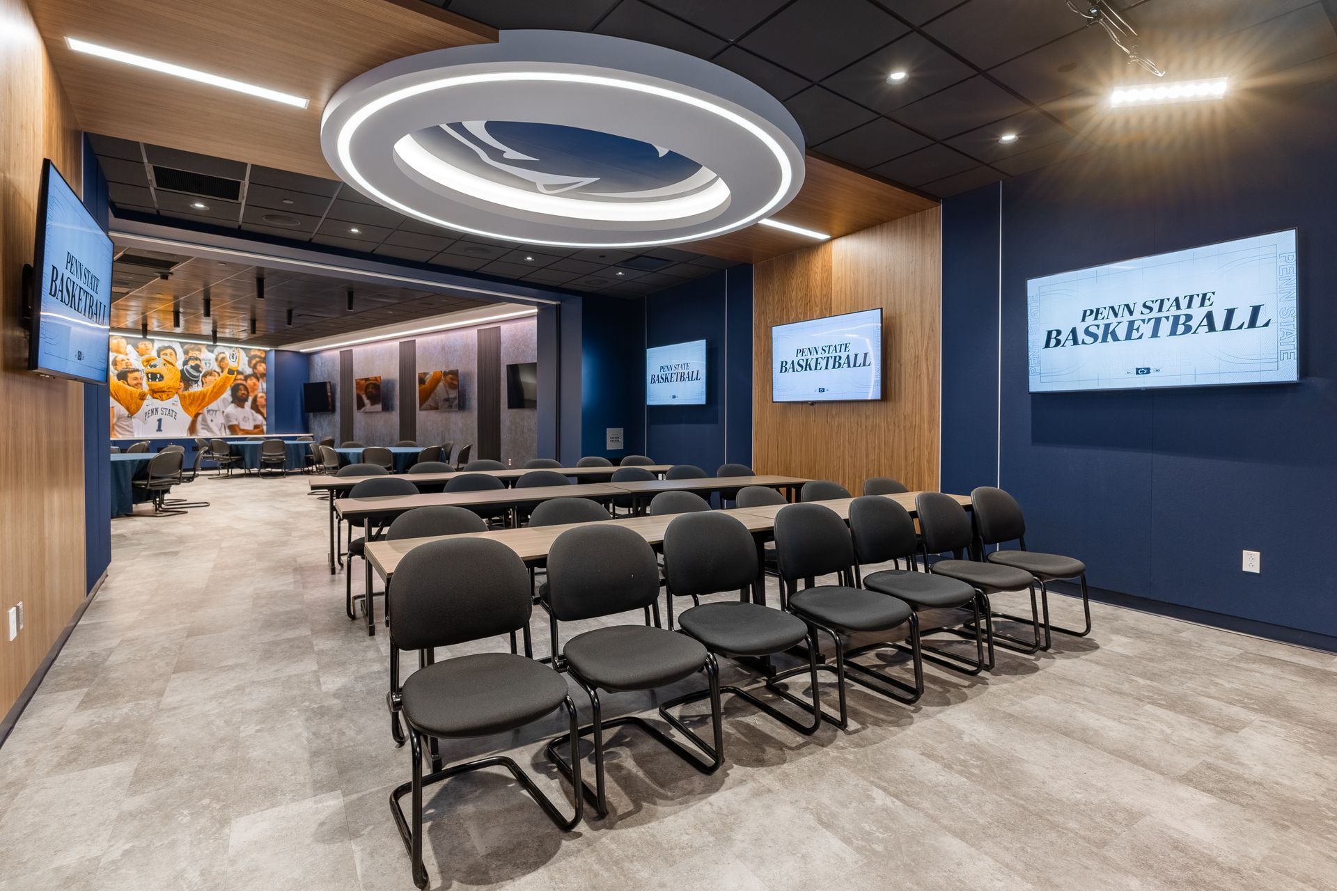 Bryce Jordan Center's modern conference room with rows of black chairs, a round ceiling light, and wall-mounted screens