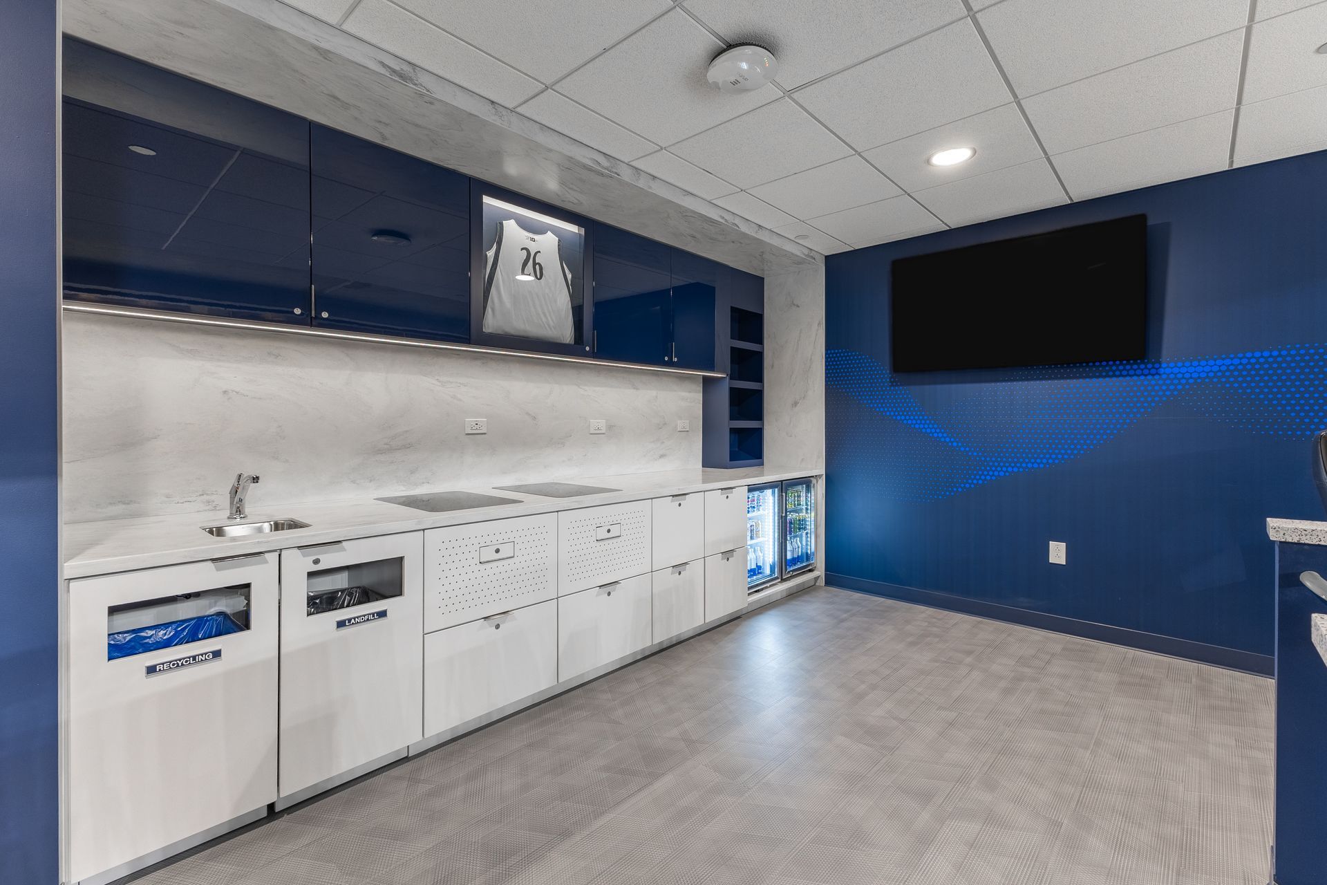 Bryce Jordan Center's modern lounge with white cabinets, gray floor, blue accent wall, and a wall-mounted TV