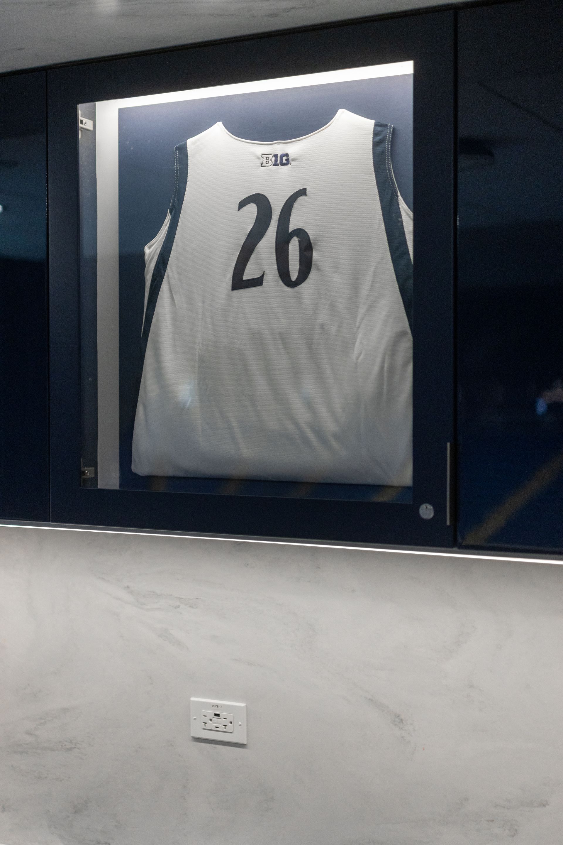 Bryce Jordan Center's framed white basketball jersey with number 26 displayed on a dark wall.