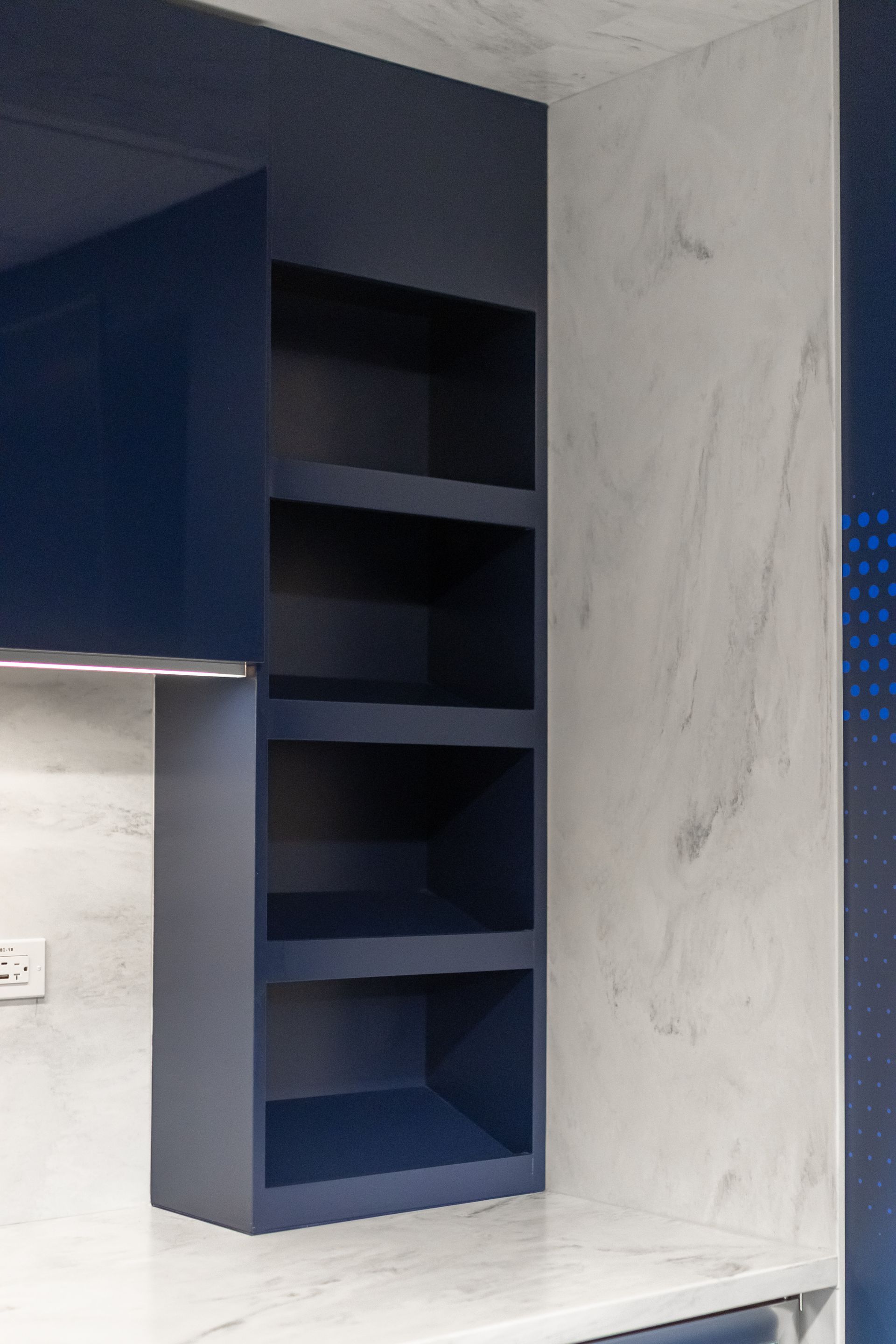 Bryce Jordan Center's modern kitchen with dark blue open shelves beside a white marble-look wall, and a sink below on the left