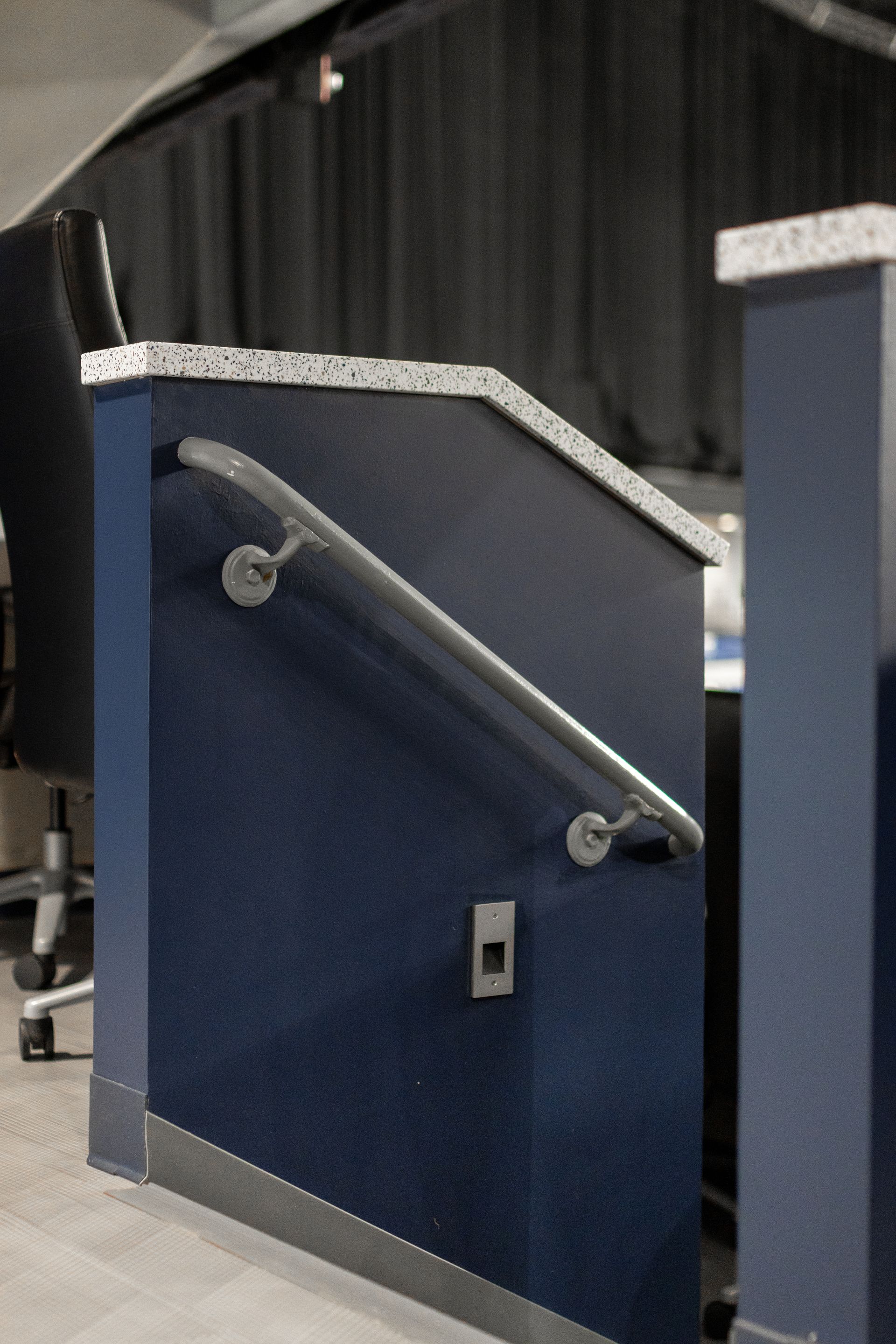 Bryce Jordan Center's blue metal barrier with a diagonal handrail on a carpeted indoor staircase landing