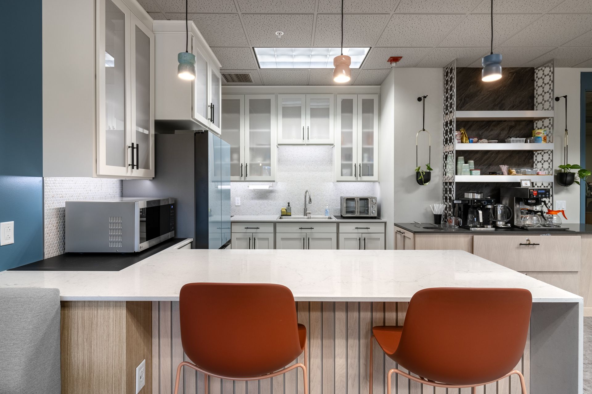 Penn State Earth and Engineering Sciences kitchen with white cabinets, a large white island with two orange chairs, and a coffee station.