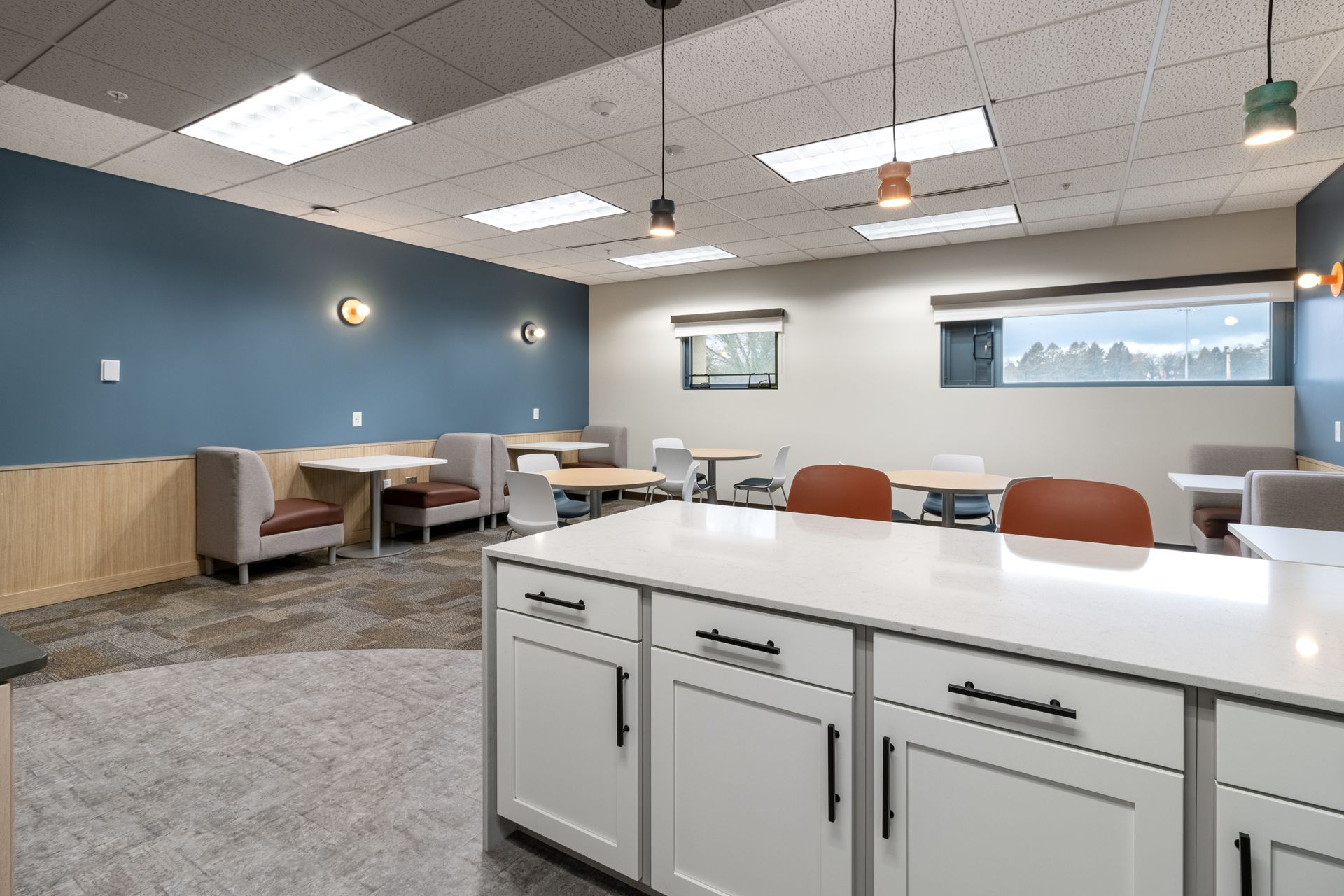 Penn State Earth and Engineering Sciences kitchen with white kitchen cabinets in the foreground, dining booths against a blue wall, and tables.
