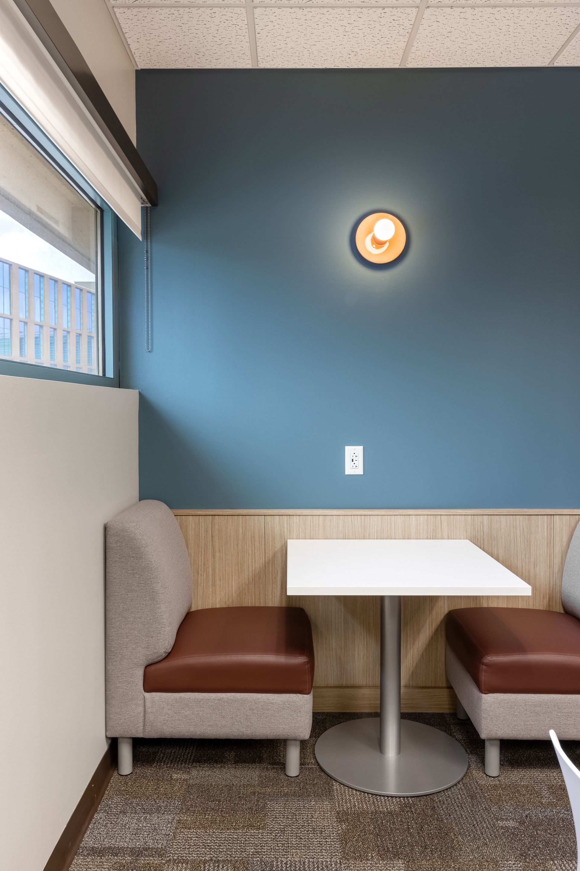 Penn State Earth and Engineering Sciences kitchen with a blue wall, two brown-cushioned seats, a white square table, and a circular wall light.