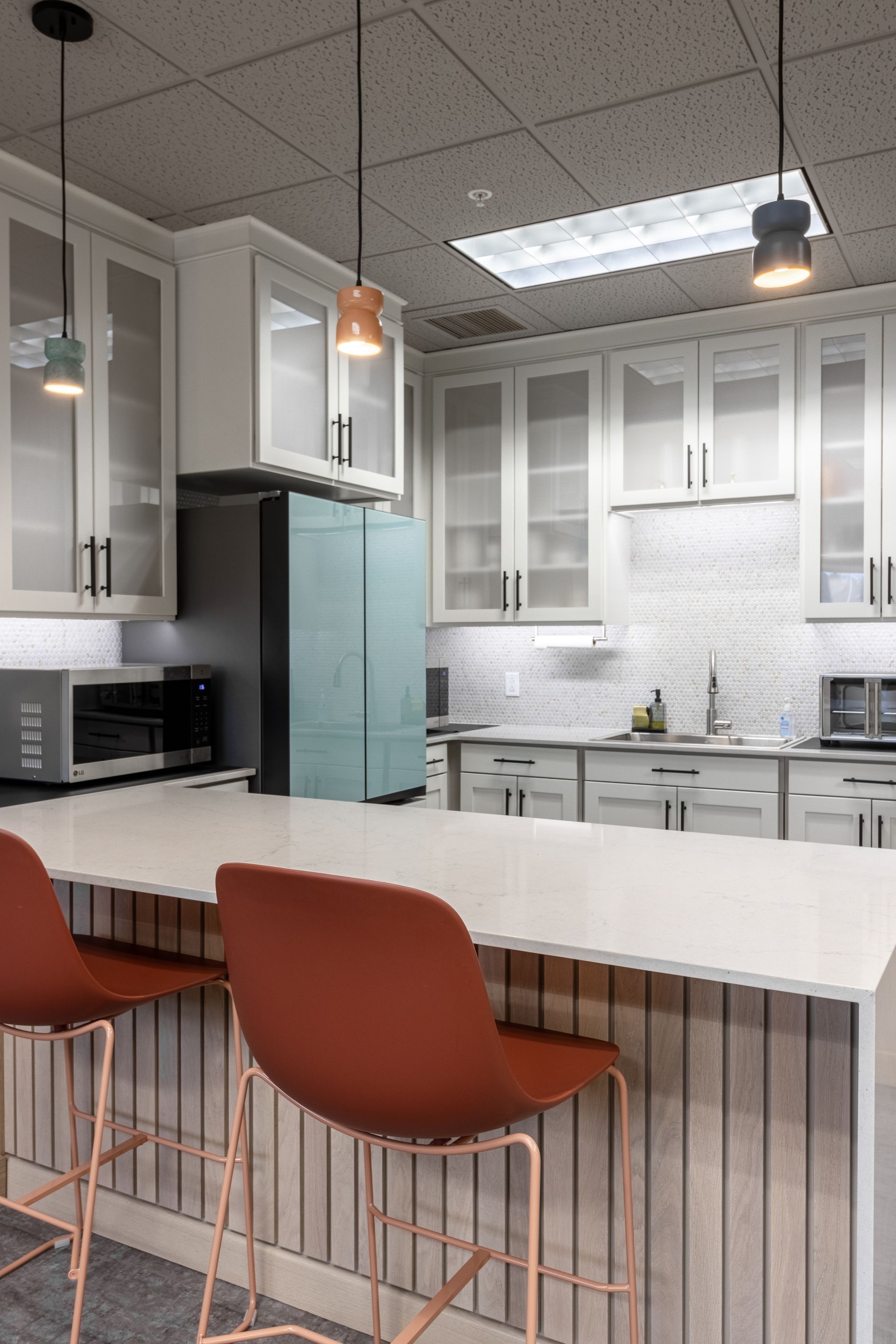 Penn State Earth and Engineering Sciences kitchen featuring white cabinets, a light-blue refrigerator, two rust-colored bar stools, and a quartz countertop.