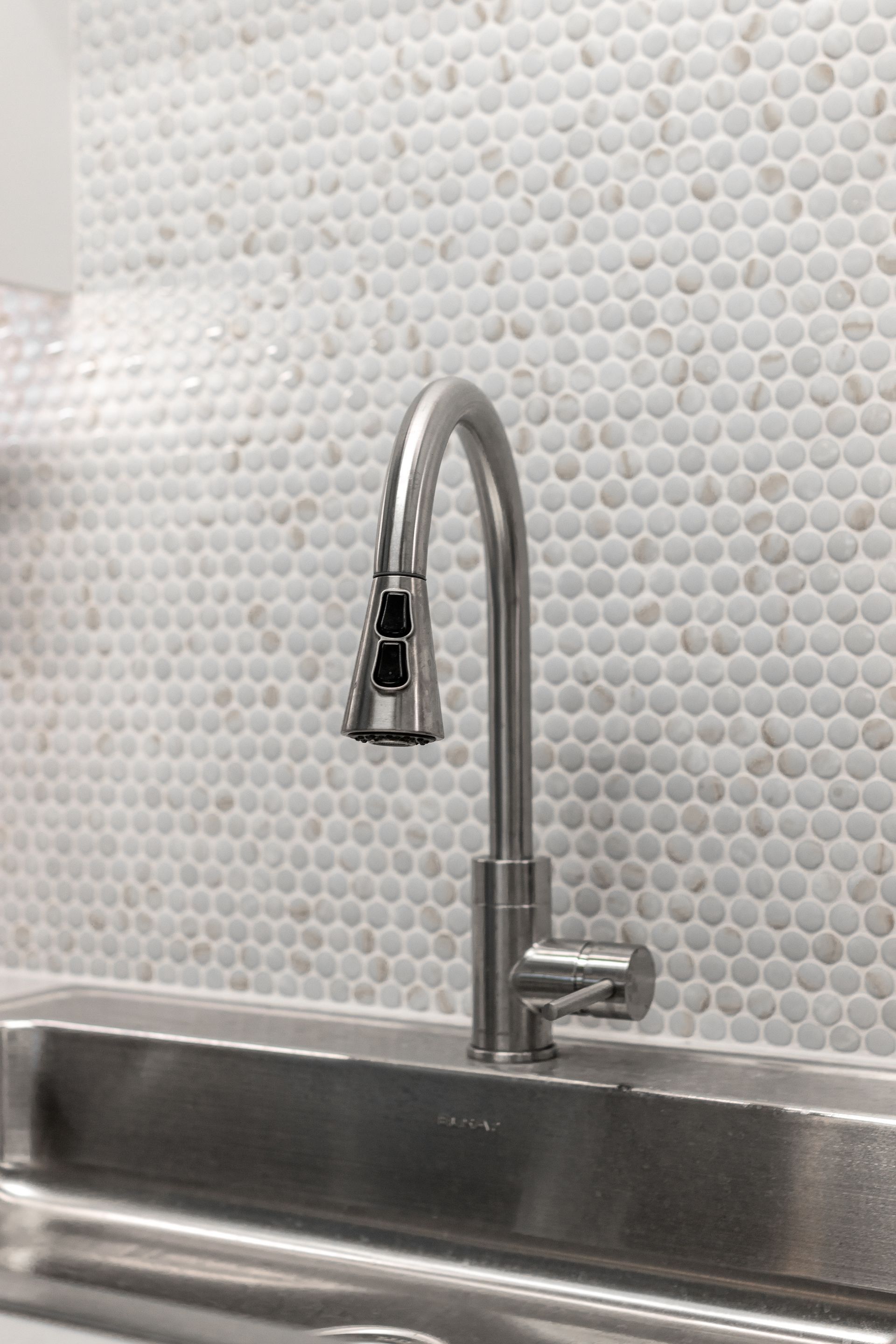 Penn State Earth and Engineering Sciences kitchen's brushed-nickel pull-down faucet installed against a white penny-round tiled backsplash.