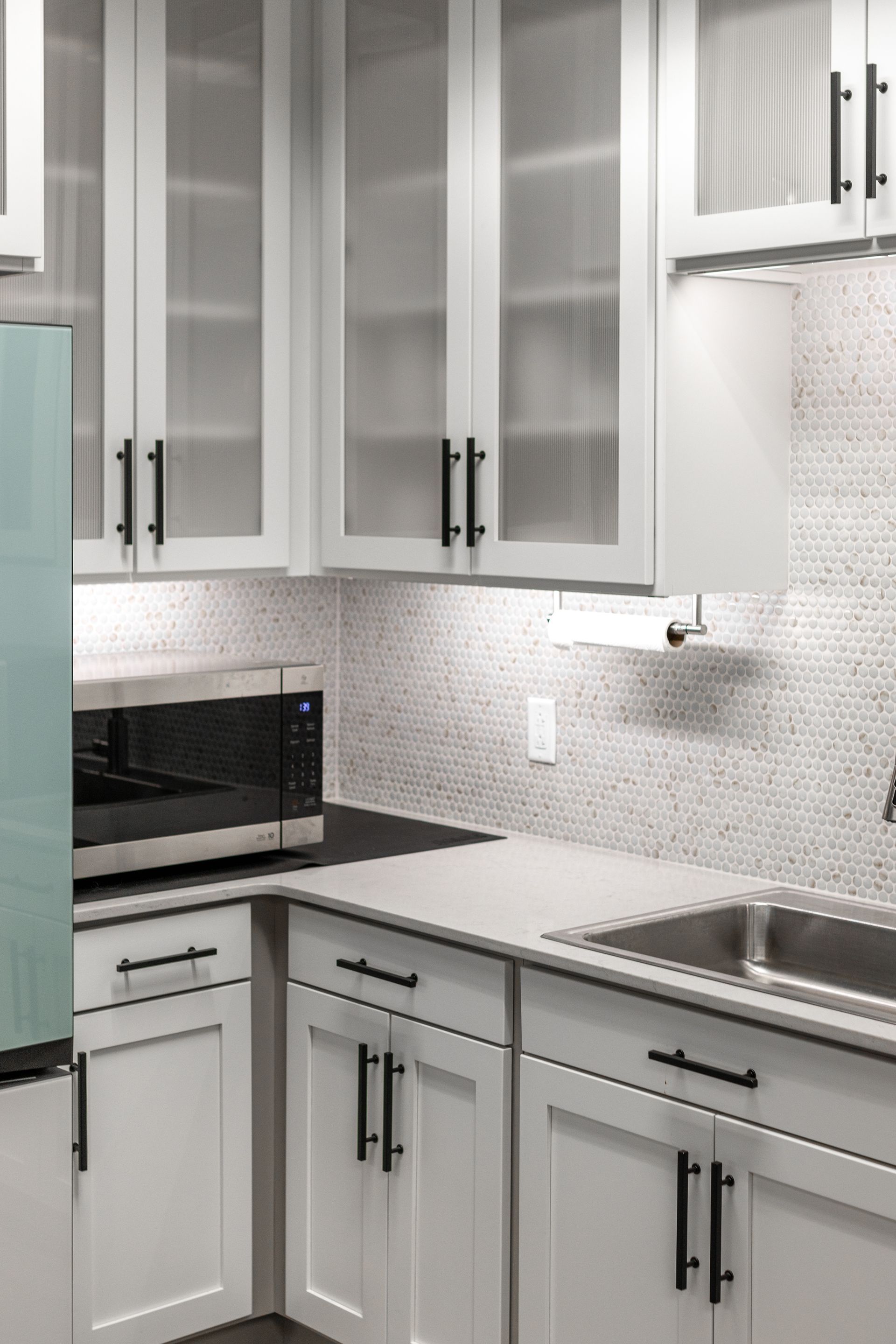 Penn State Earth and Engineering Sciences kitchen with glass-front cabinets, a stainless steel microwave, and white hexagonal tile backsplash.