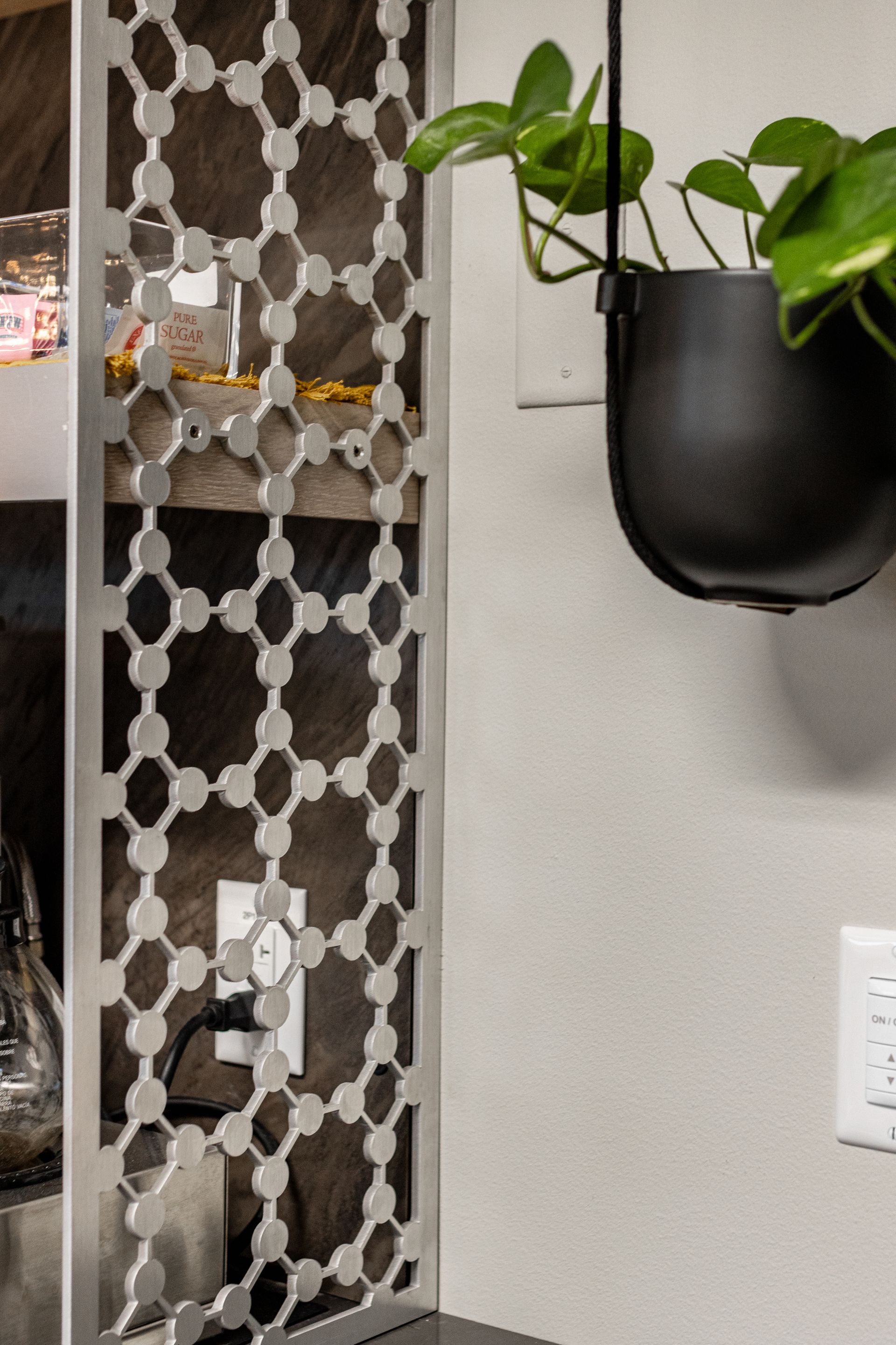 A hanging black planter with a green plant beside a silver geometric metal room divider wall at Penn State Earth and Engineering Sciences kitchen.