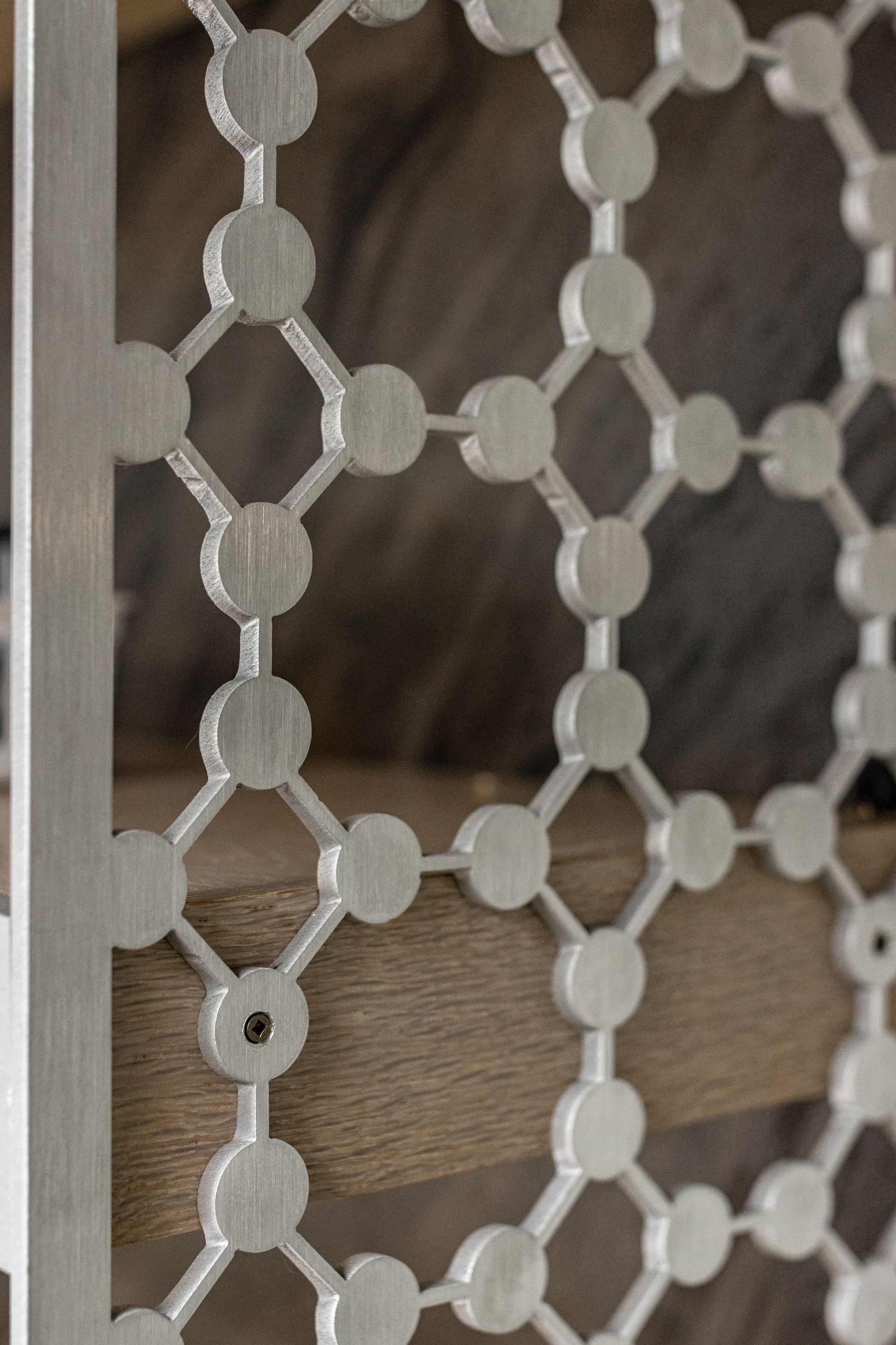 A silver, metallic screen with a repeating circular lattice pattern placed in front of horizontal wooden slats.