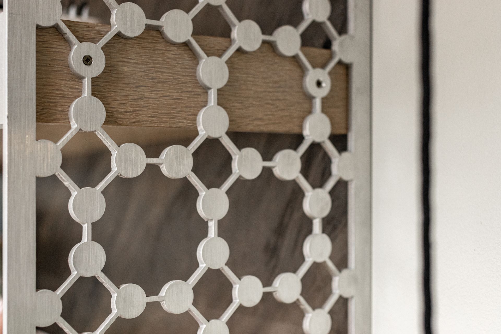 A decorative silver metal lattice screen with a geometric circular pattern over a textured wooden surface.