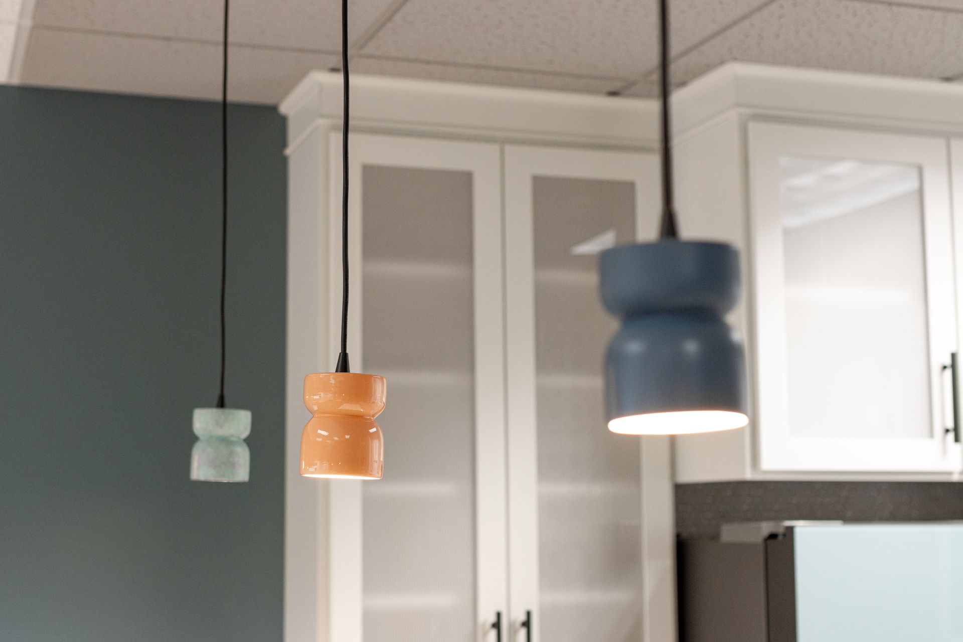 Three pendant lights in mint, orange, and navy blue hang in front of white kitchen cabinets at Penn State Earth and Engineering Sciences kitchen.