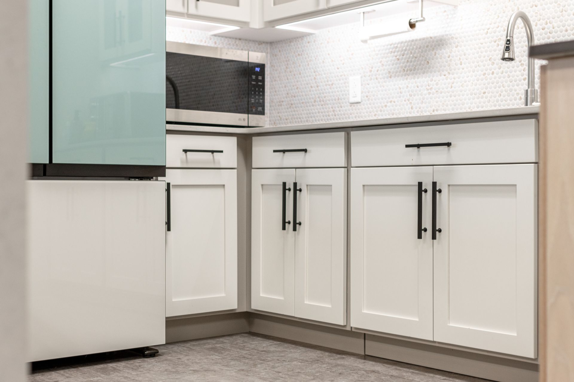 A modern kitchen corner featuring white shaker-style cabinets with black hardware, a microwave, and a tiled backsplash.