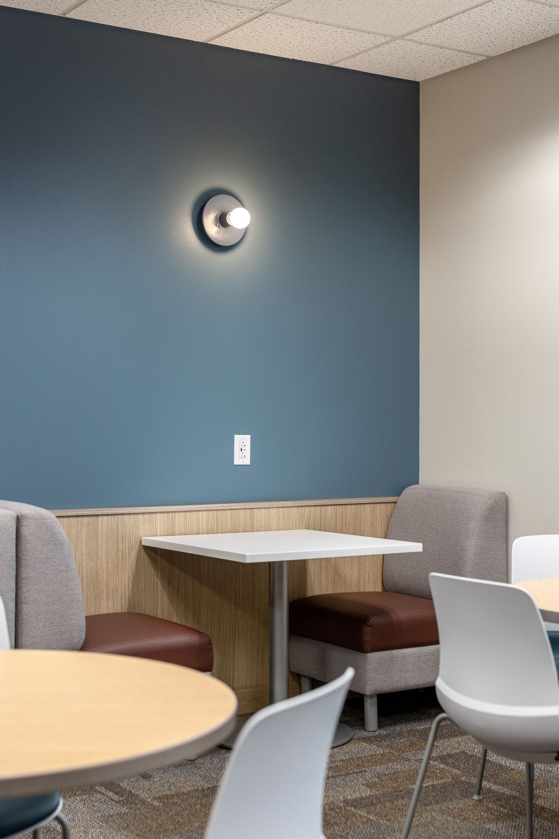 A cafe-style seating area with a blue accent wall, a wall-mounted light, a table, and upholstered chairs.