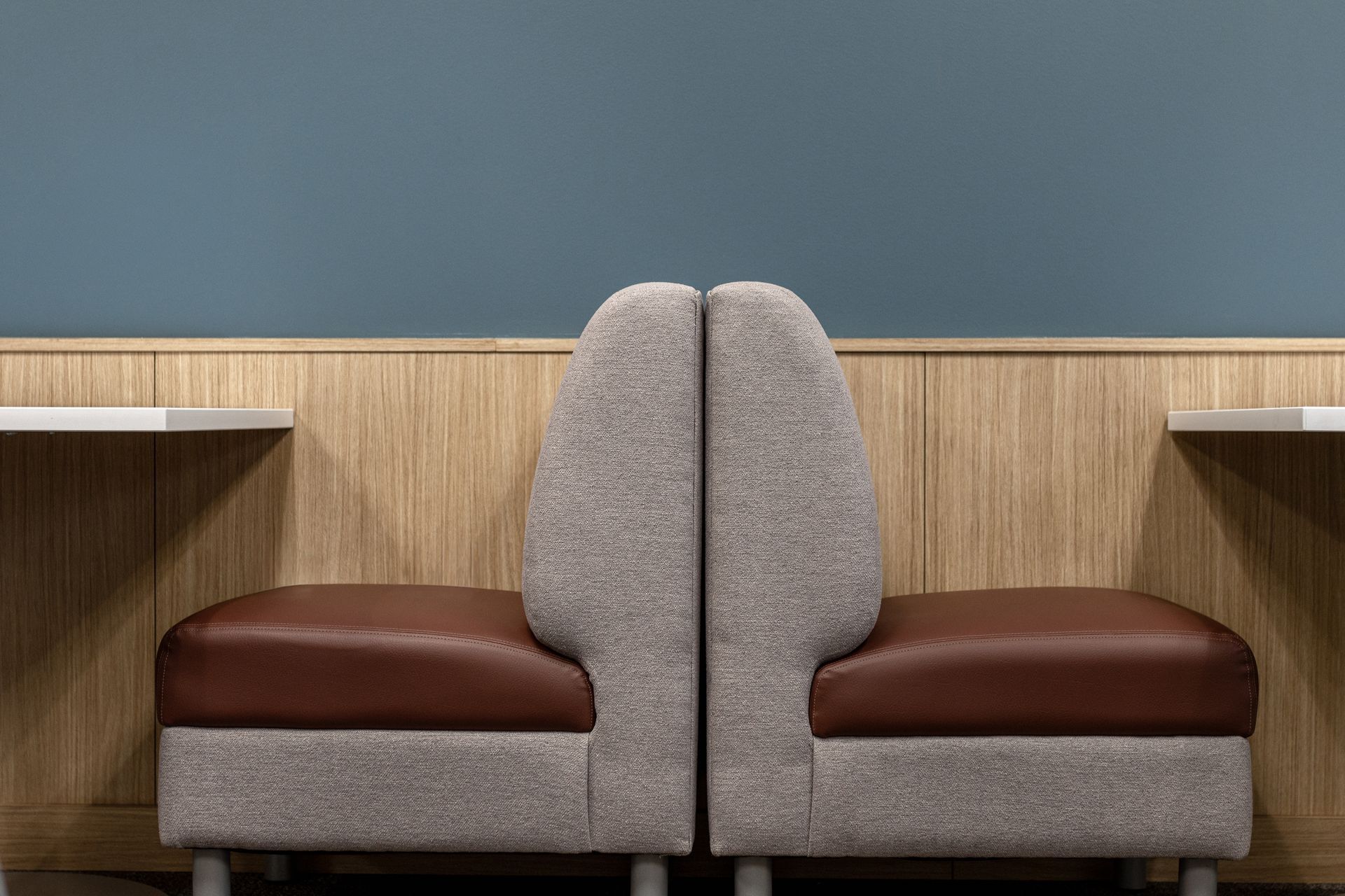 Two back-to-back booth seats with brown vinyl cushions and grey textured fabric, set against a wooden wall and blue background.