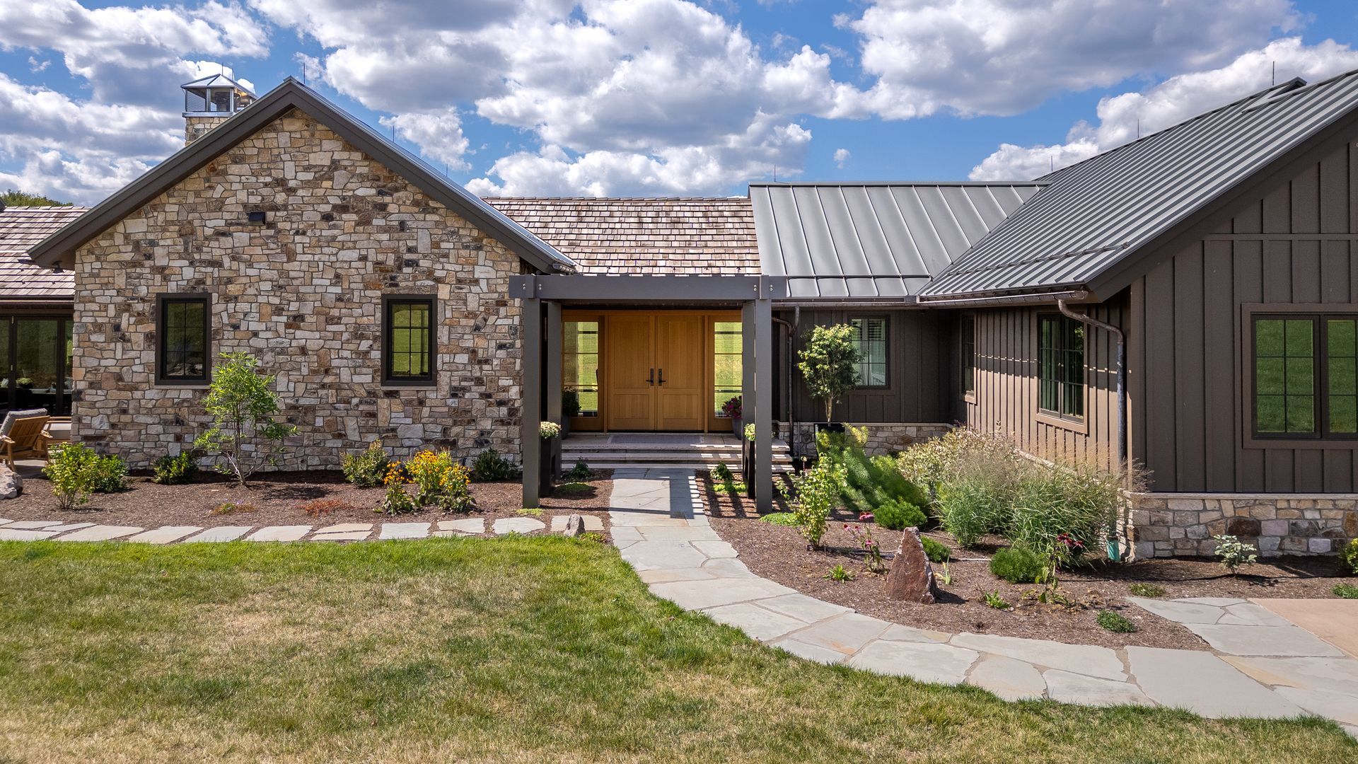 Stone house exterior with a metal roof, front walkway, and landscaped yard under a cloudy sky