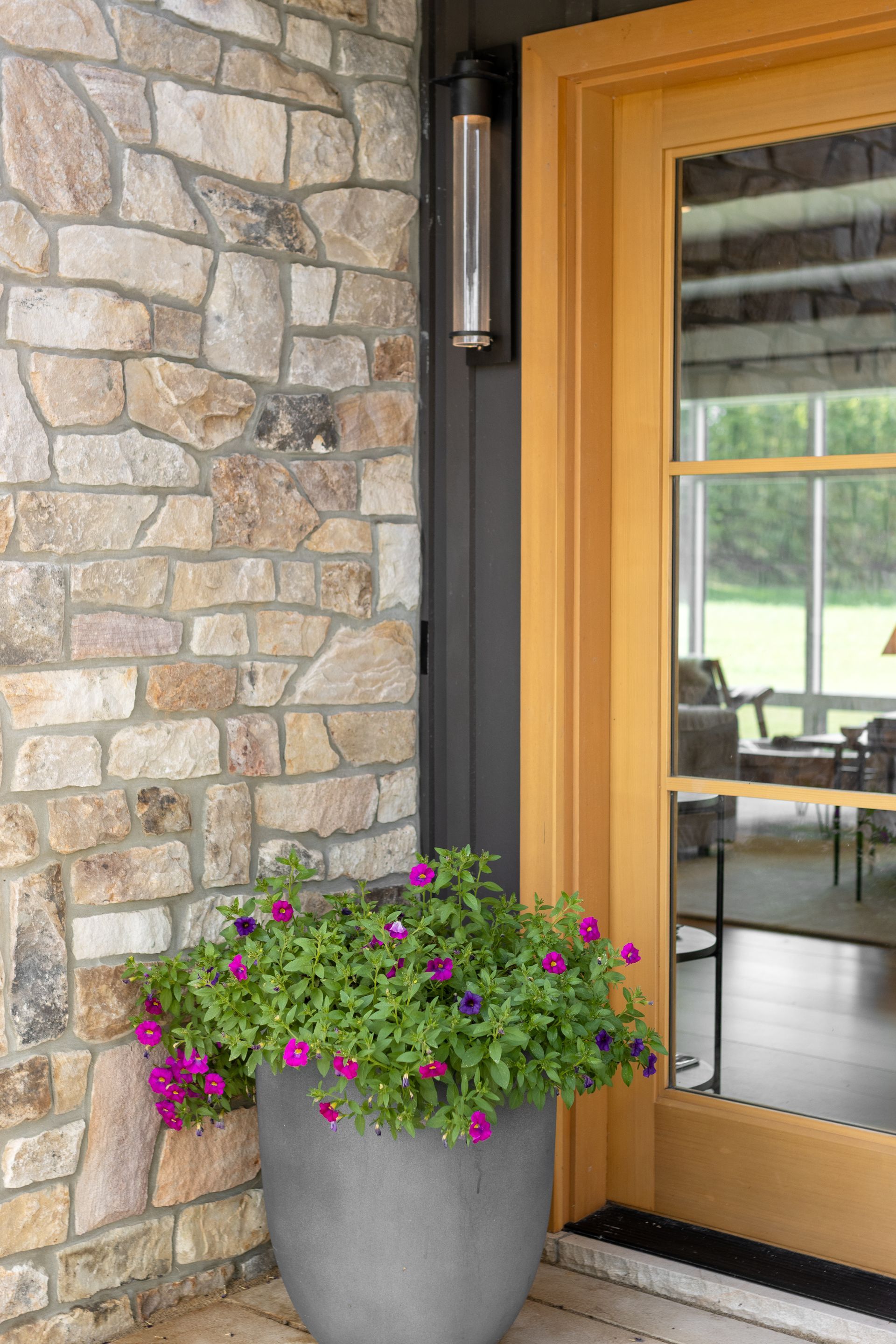 A potted plant with small purple flowers sits next to a glass door with a wood frame and a stone exterior wall.