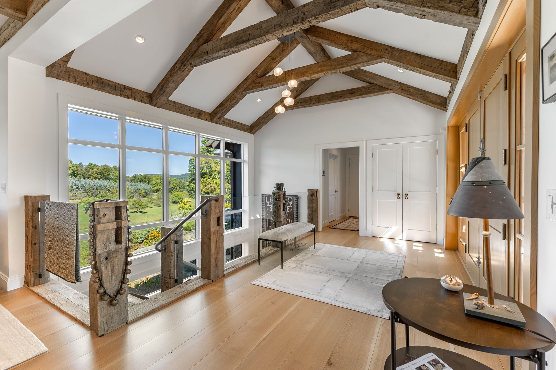 A bright, modern entryway with exposed wooden ceiling beams, light hardwood floors, a bench, and large floor-to-ceiling windows.