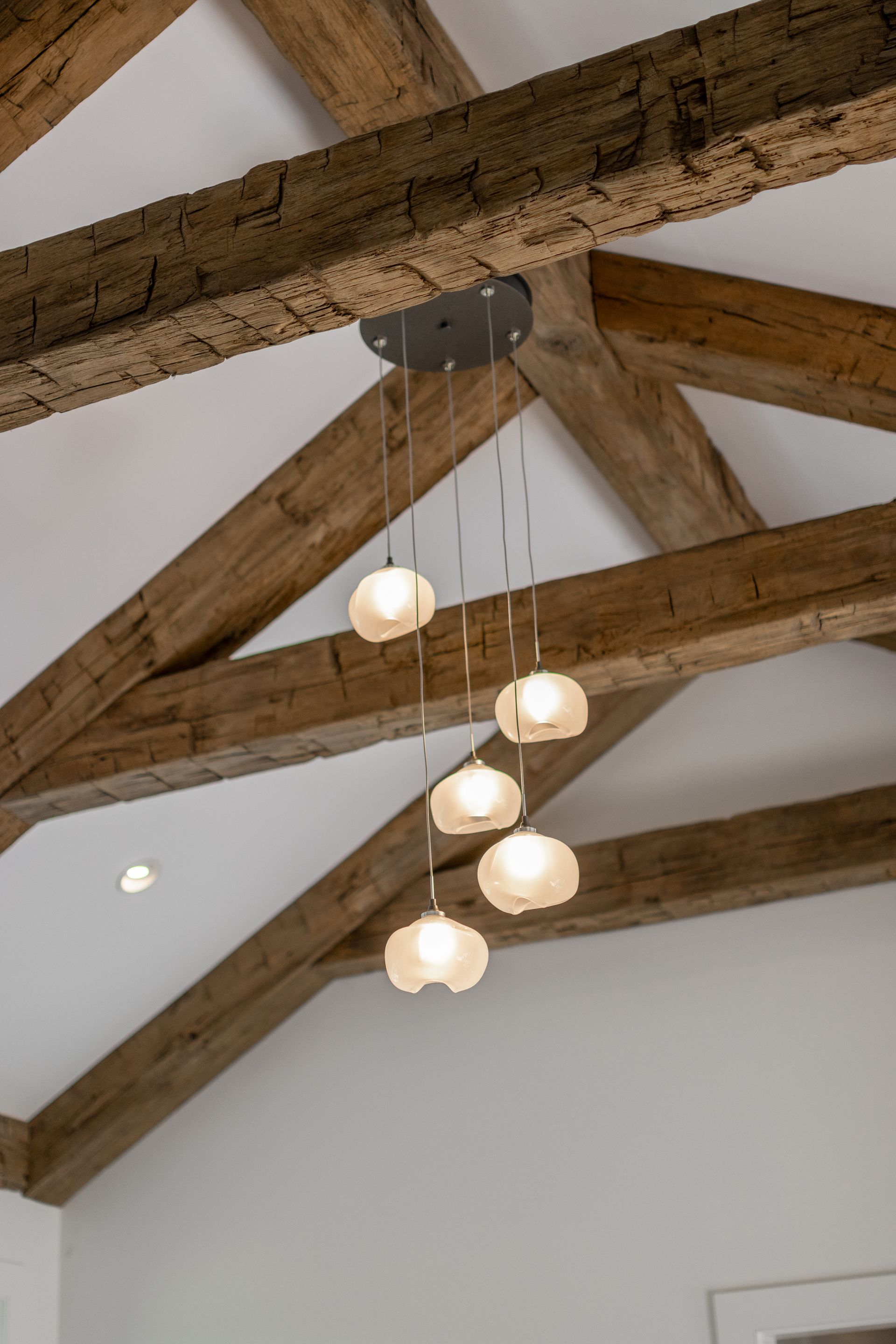 A modern multi-light pendant fixture hangs from a white ceiling with rustic, exposed wooden beams.